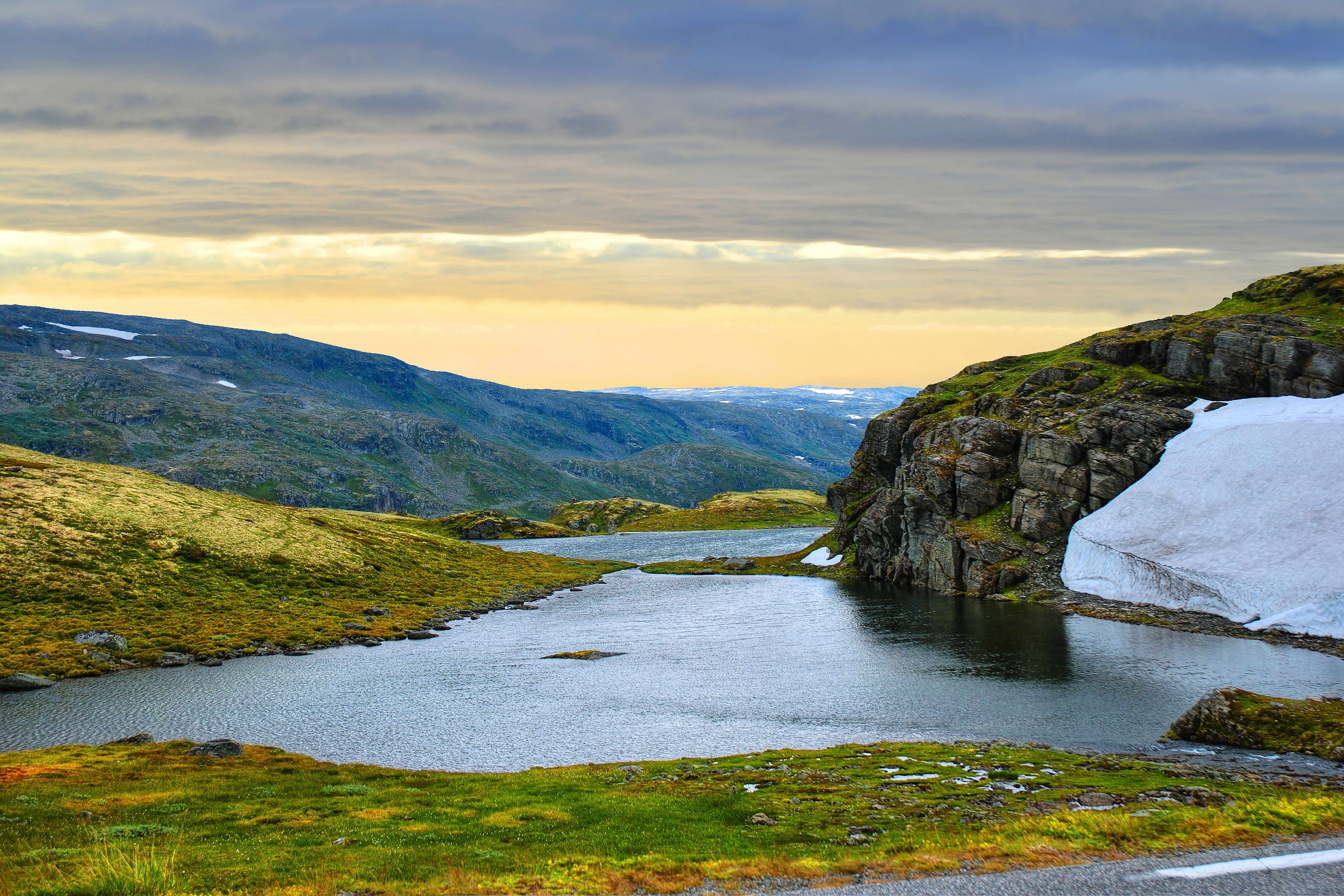 Fredelig bjergsø på Hardangervidda-plateauet i Norge omgivet af snepletter, grønne bakker og dramatiske skyer