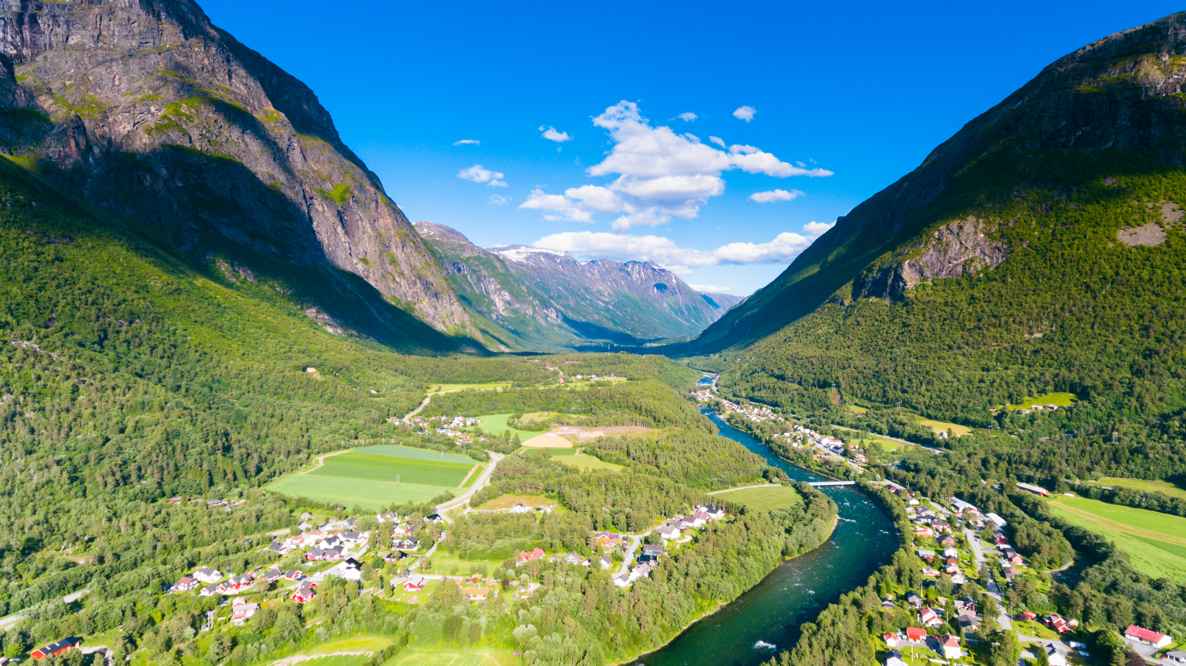 Fantastisk norsk fjeldlandskab med grøn dal, meandrerende flod og traditionel landsby