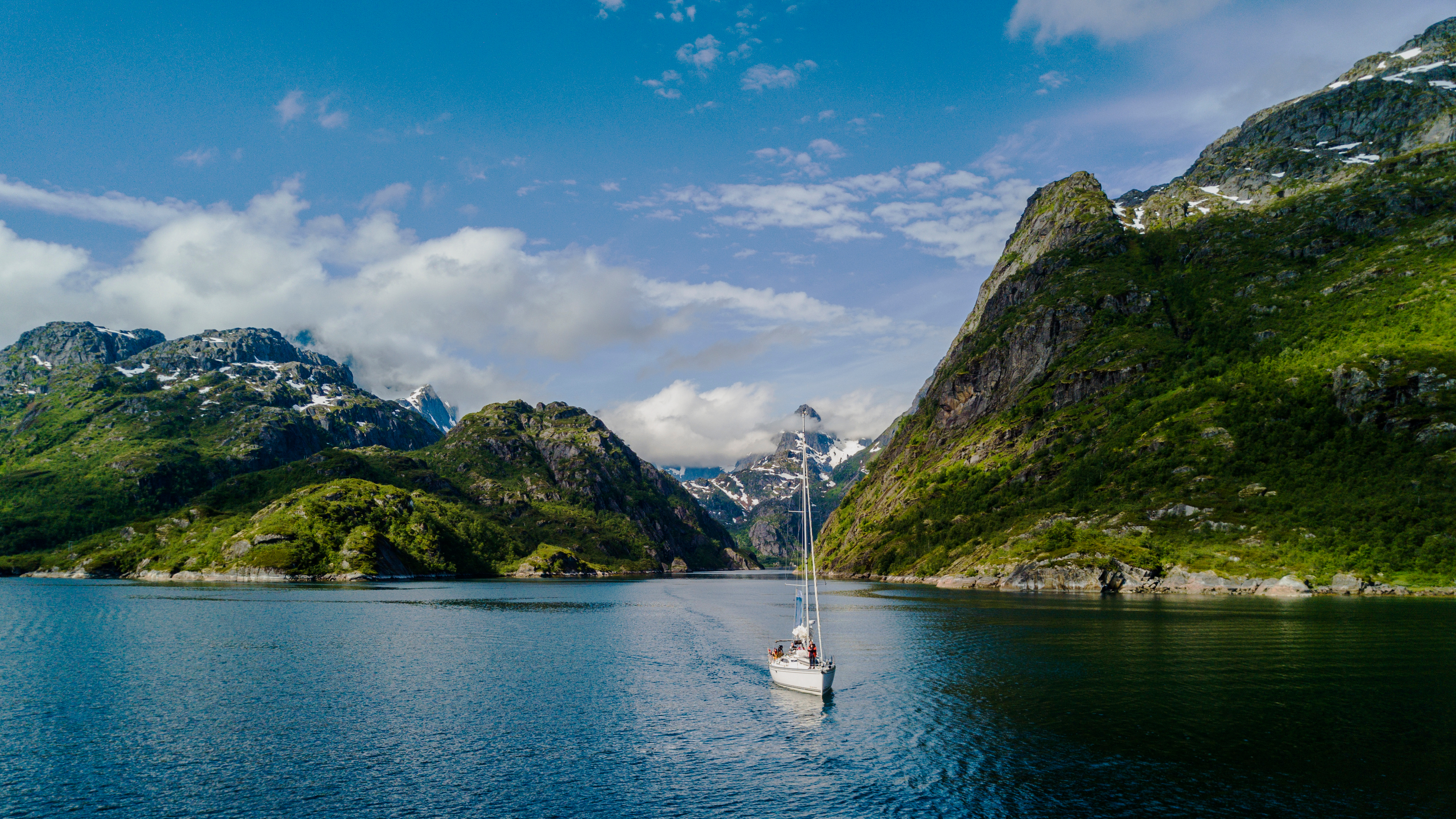 Sejlbåd på rolig fjordsejlads i Trollfjord Norge omgivet af storslåede grønne bjerge med sne og spejlblank vandflade