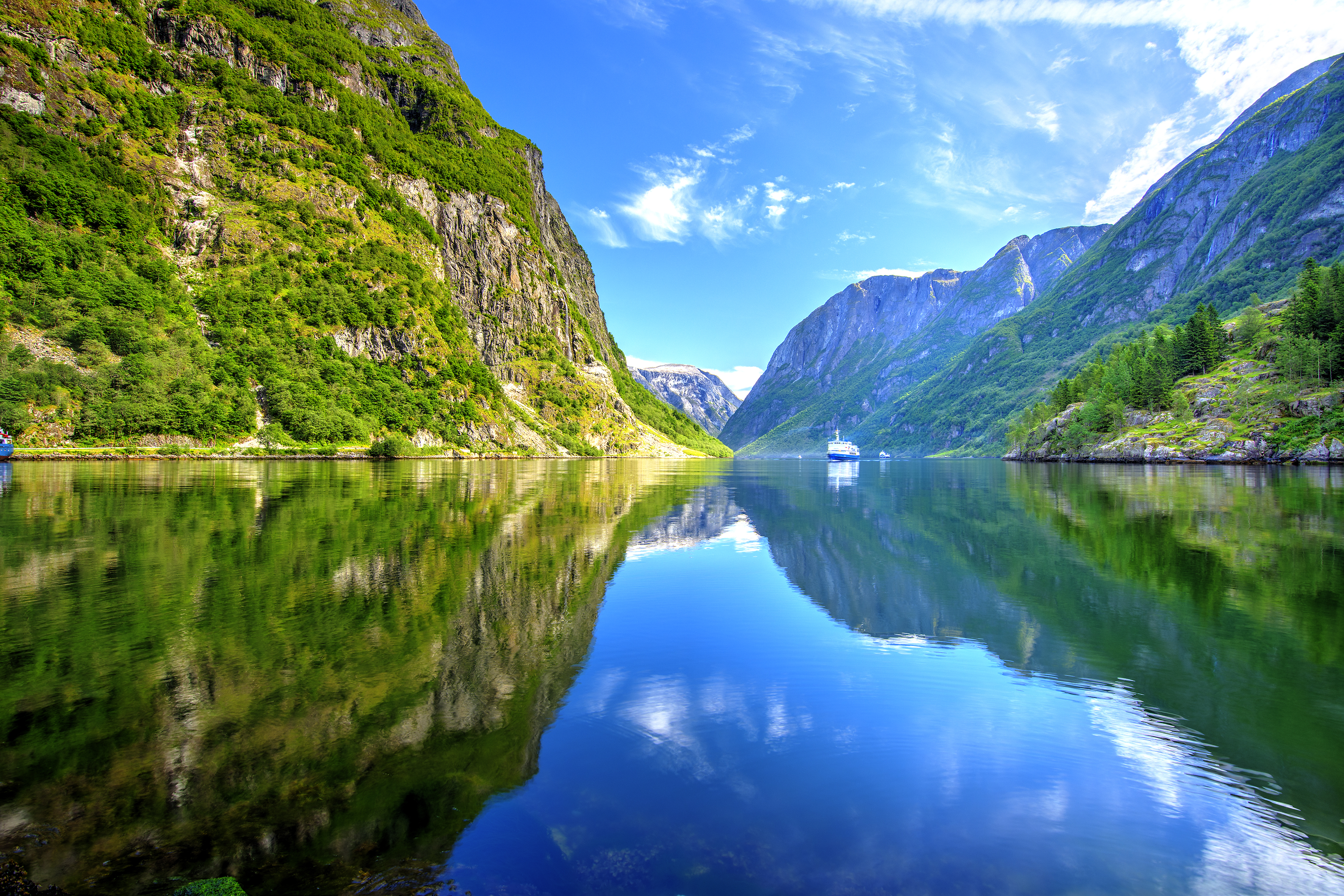 Idylliske norske fjorde med glasklart vand, imponerende bjergformationer og krydstogtskib omgivet af grøn natur
