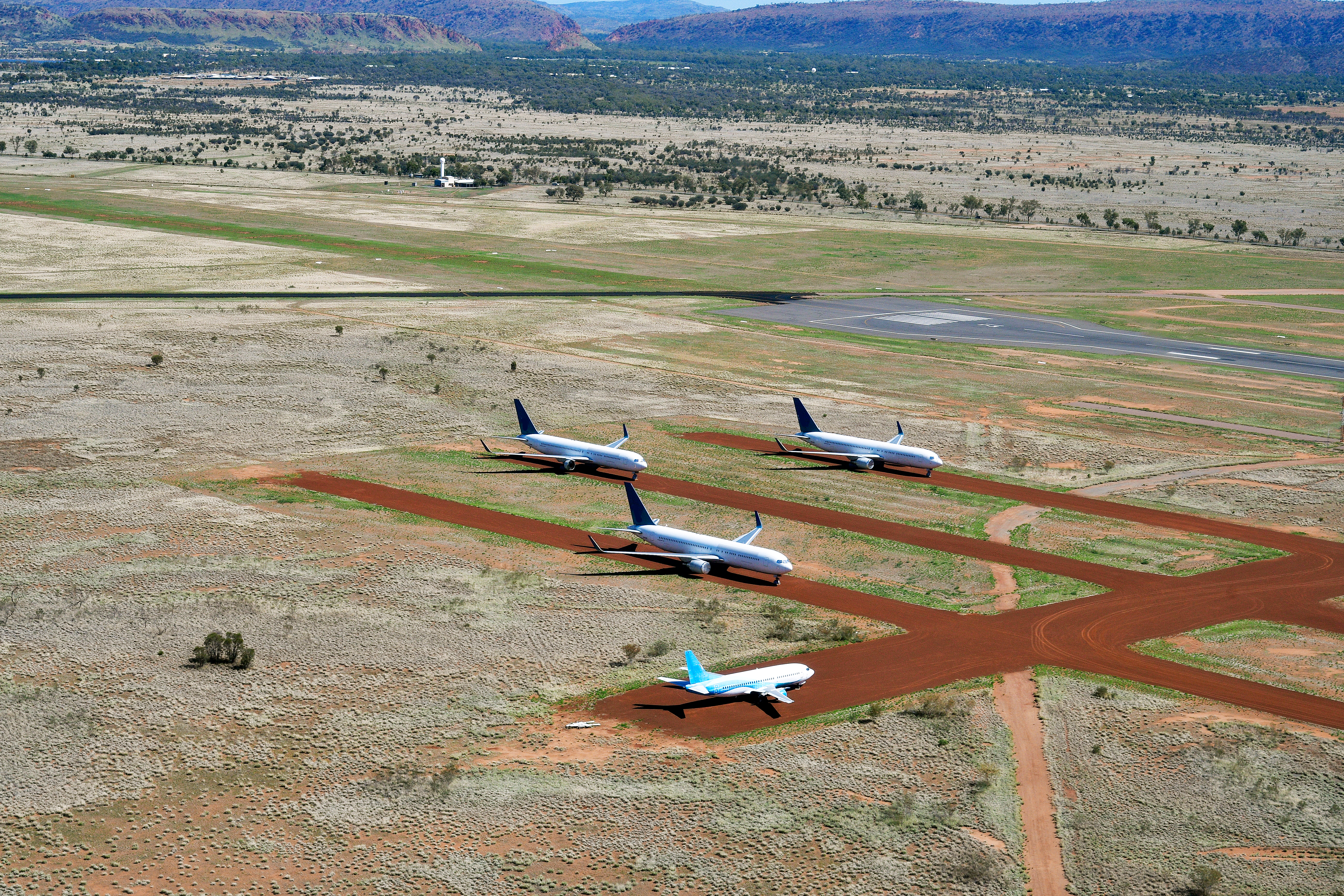 Flyvemaskiner på standpladsen ved Alice Springs lufthavn med den ikoniske røde jord i Australiens Northern Territory