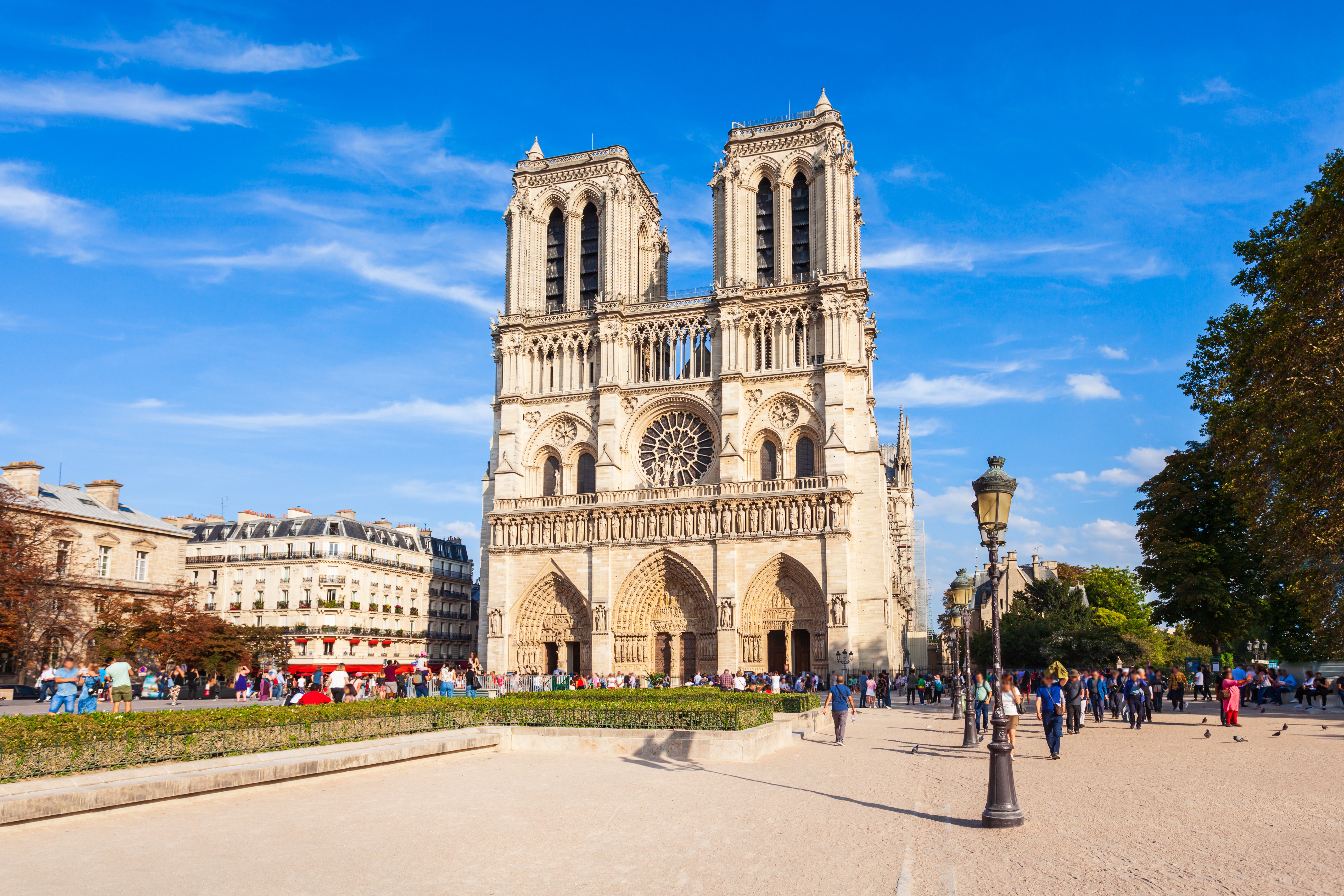 Den berømte Notre-Dame Katedral i Paris fotograferet forfra med turister på pladsen og blå himmel i baggrunden