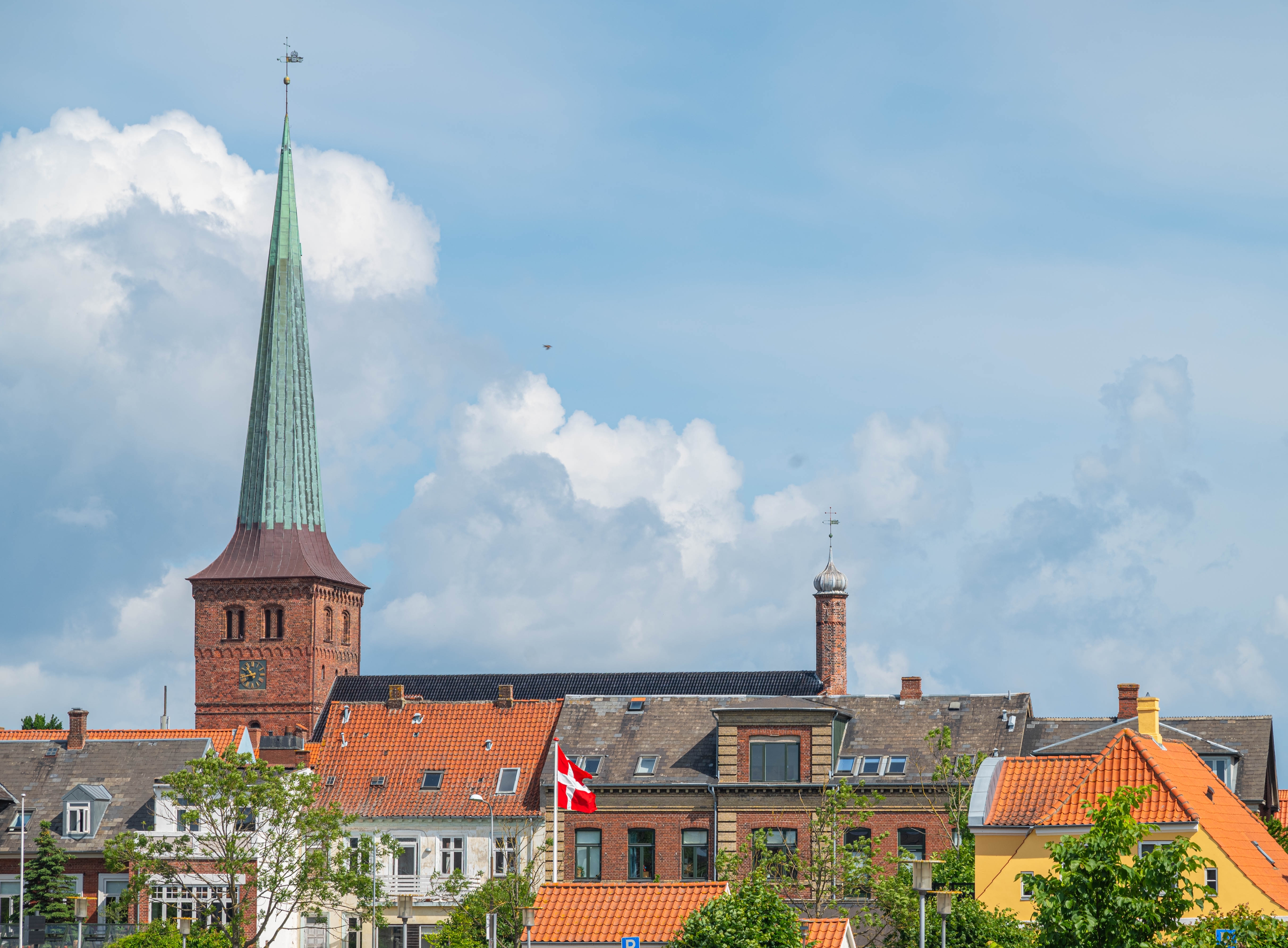Idyllisk sommerbillede af Nyborg med historisk kirke og røde tegltage med Dannebrog mod blå himmel på Fyn