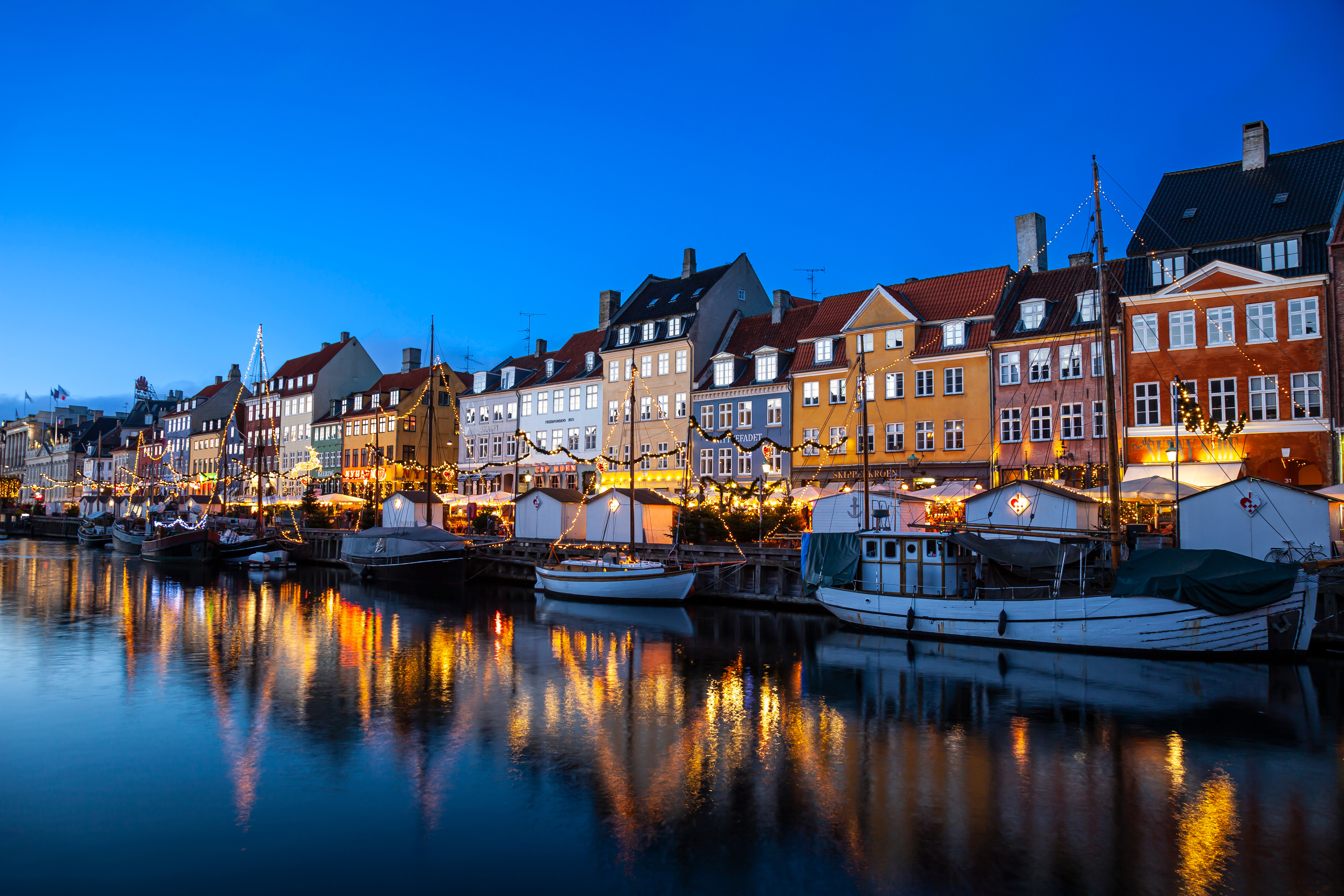 Julemarked ved Nyhavn i København med festlige lys og farverige bygninger reflekteret i den rolige kanal om aftenen