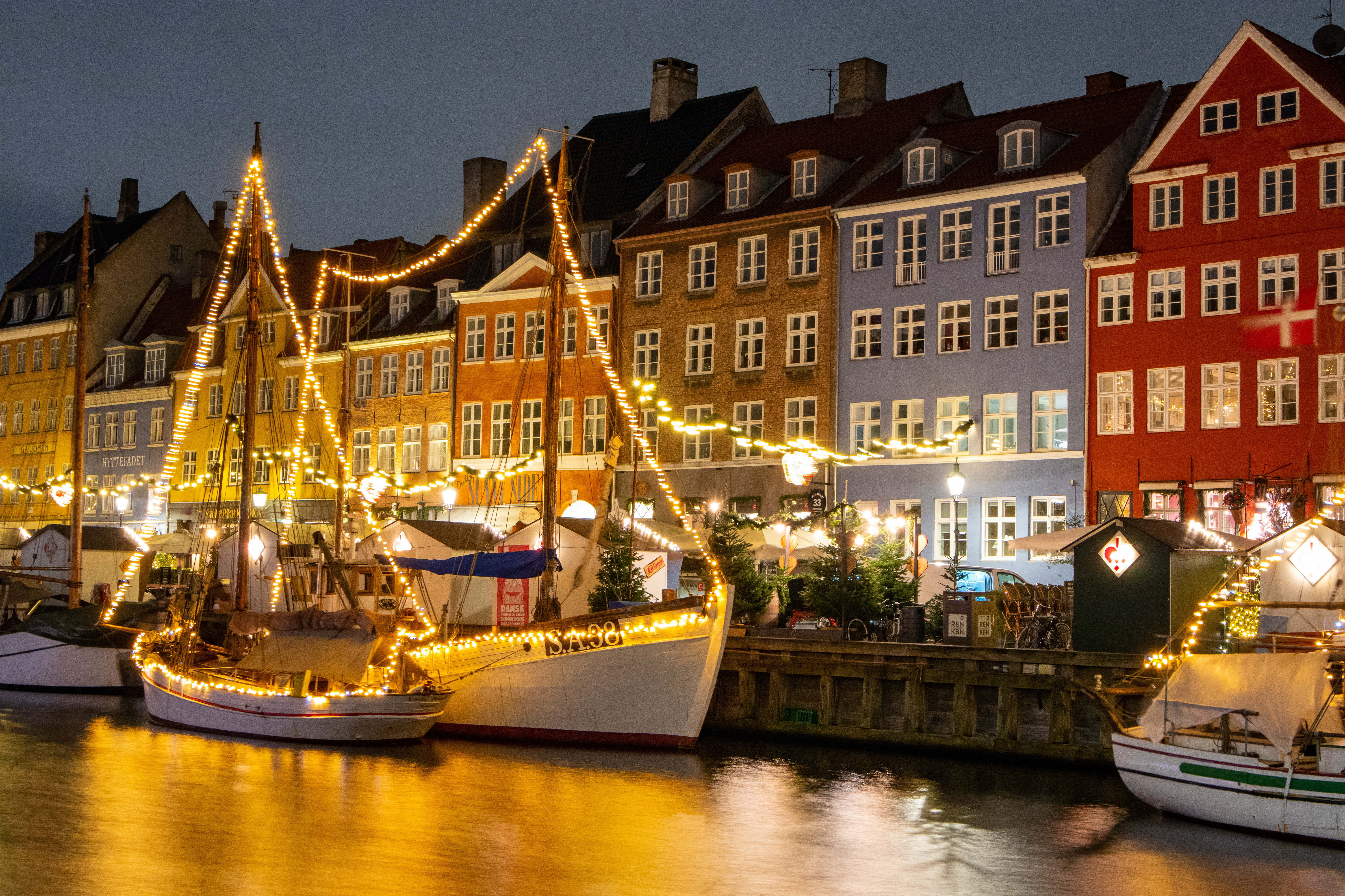 Vinterudsigt over Nyhavn i Koebenhavn med festlig julebelysning paa de farverige facader og baade i kanalen