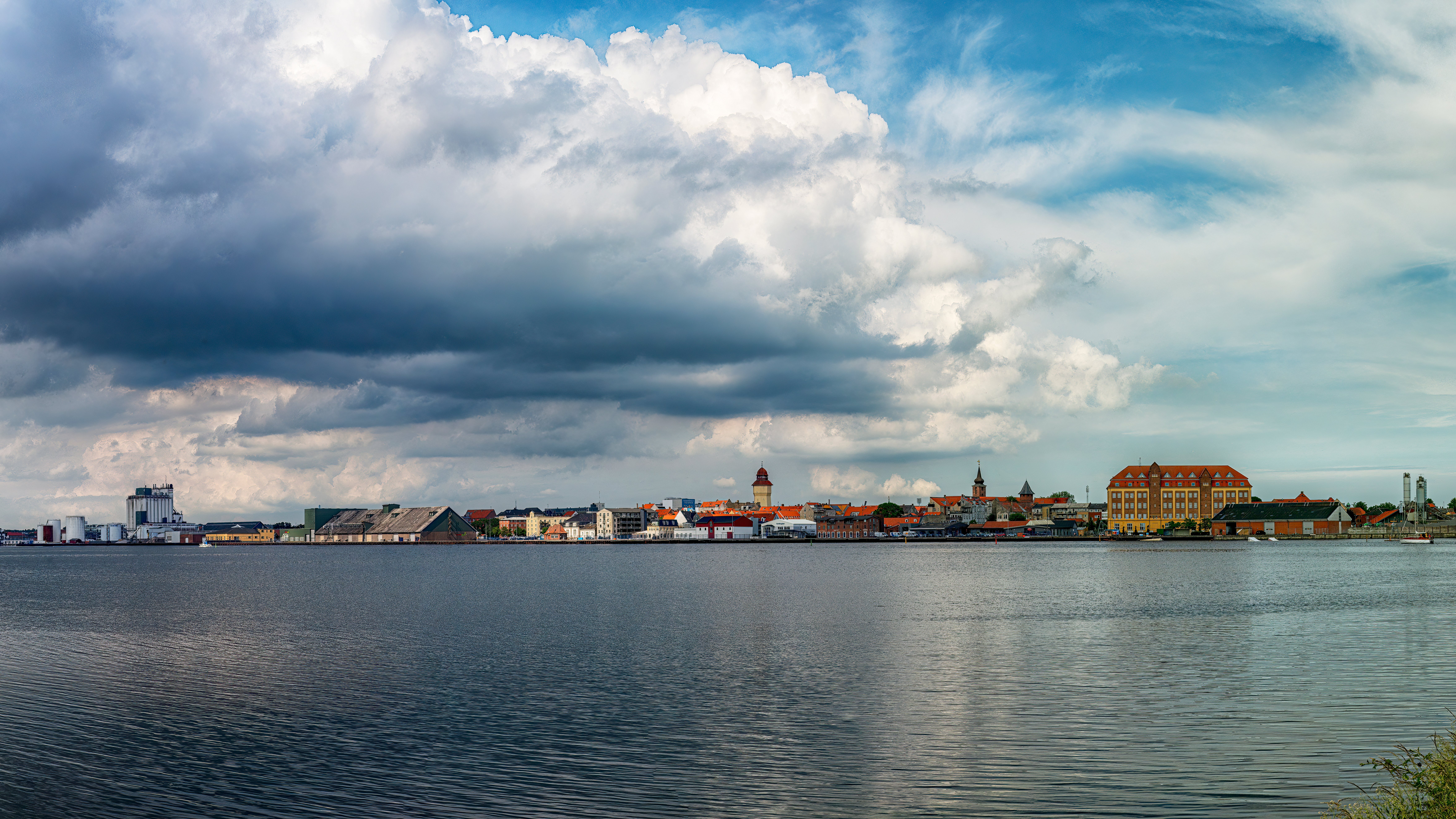 Panoramabillede af Nykøbing Falster kystlinje med historiske bygninger og dramatisk skyet himmel