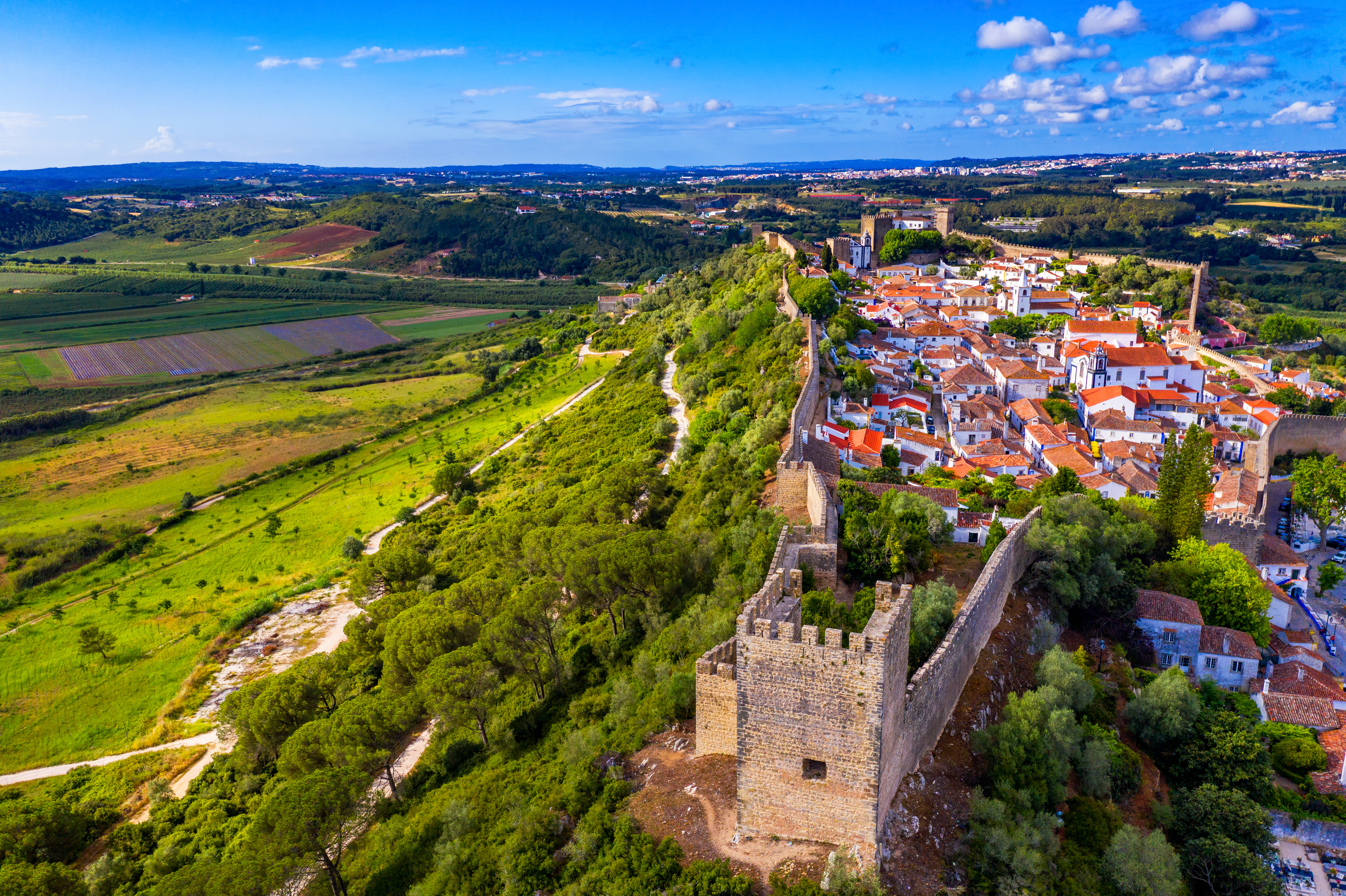 Smukt luftfoto af Óbidos i Portugal med middelalderlige bymure og fæstningstårne der omslutter den pittoreske by med hvide huse og røde tegltage