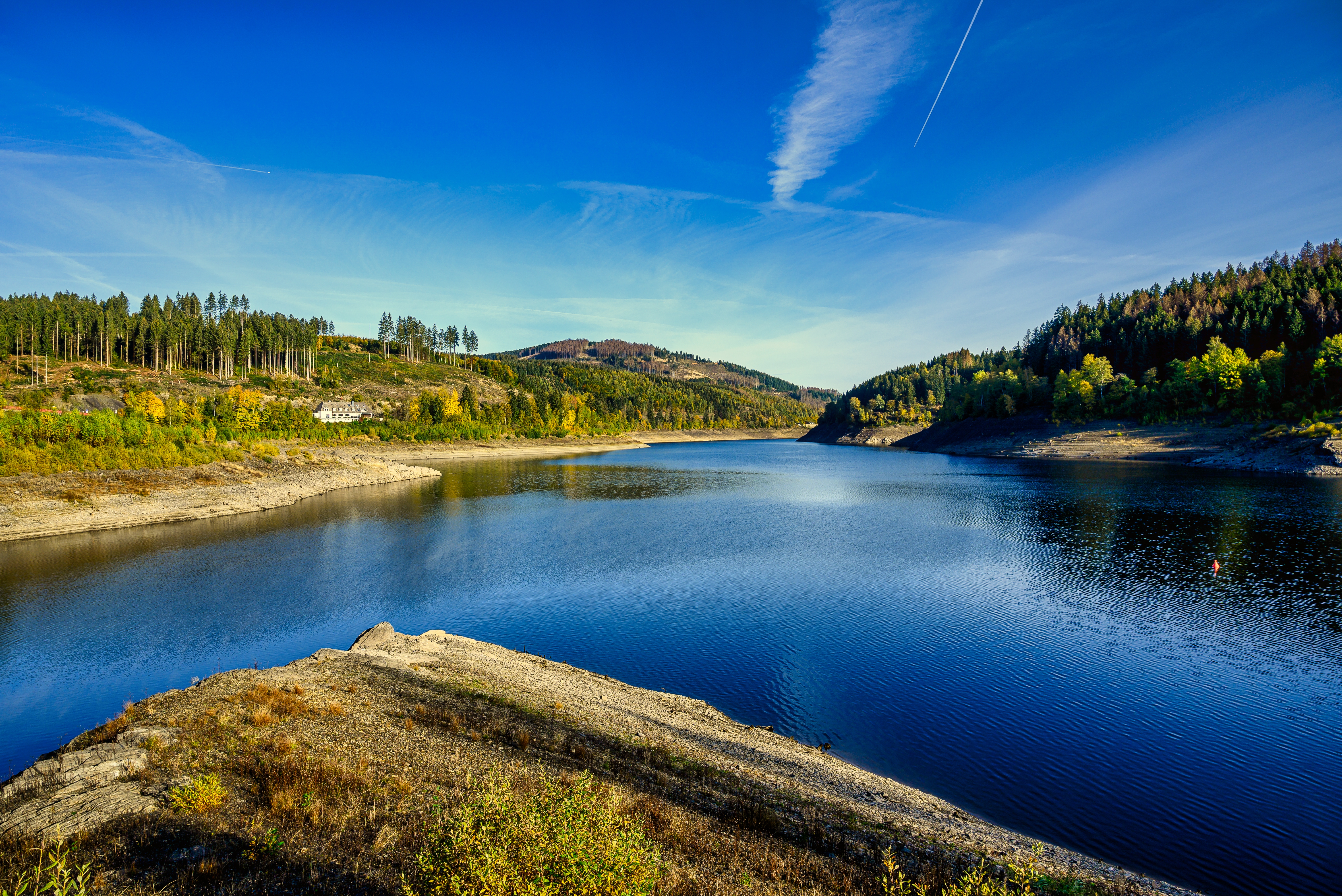 Fredfyldt naturlandskab ved Okertalsperre-reservoiret i Harz Nationalpark, Tyskland, med efterårsfarver og roligt blåt vand