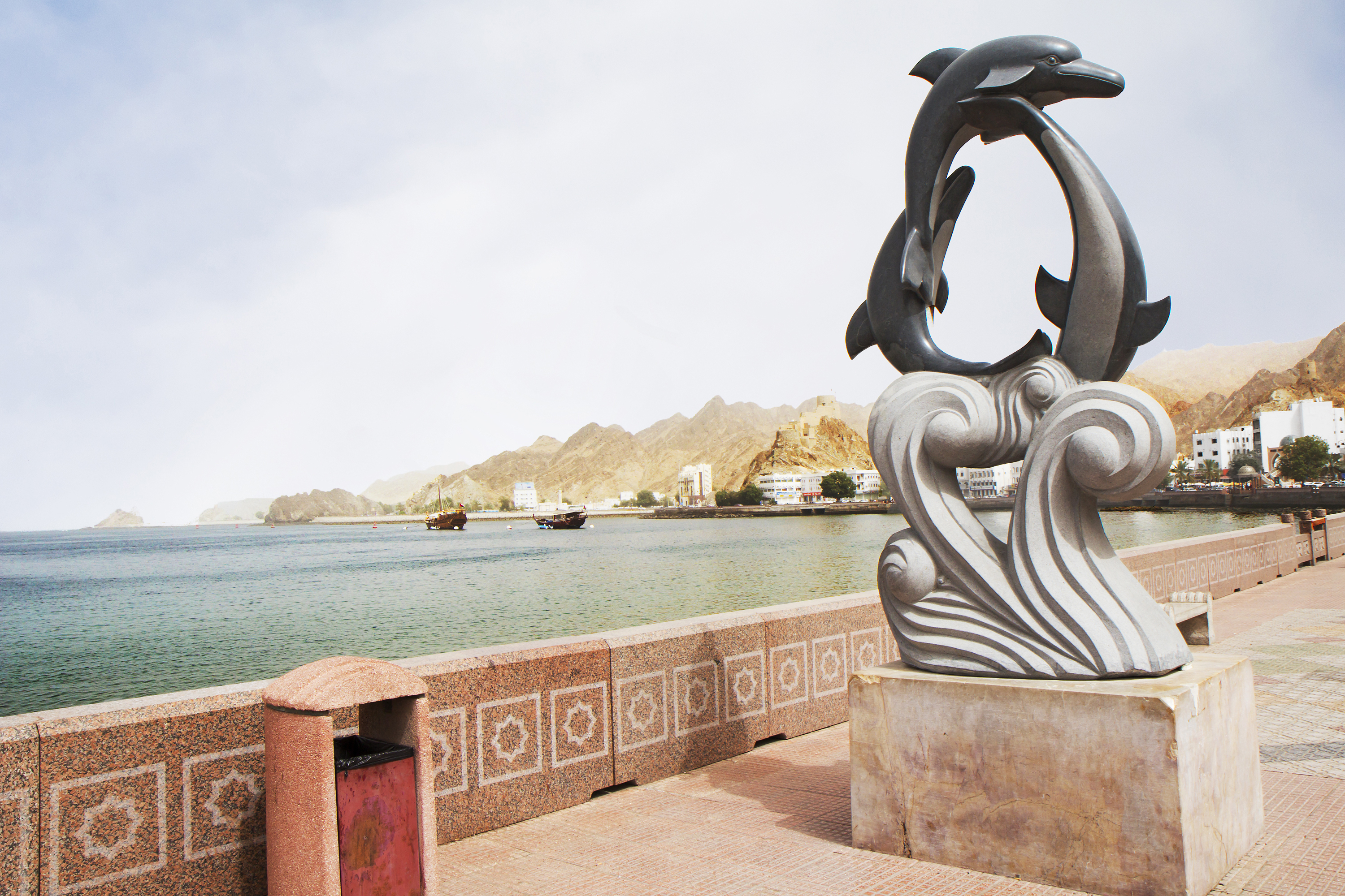 Den imponerende Corniche kystpromenade i Muscat med kunstneriske delfin-statuer og panoramaudsigt over havet og Omans bjerglandskab