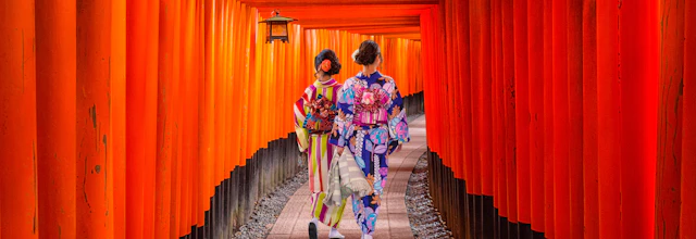 Dame i smuk kimono går gennem tunnel af orange torii-porte ved det berømte Fushimi Inari tempel i Kyoto