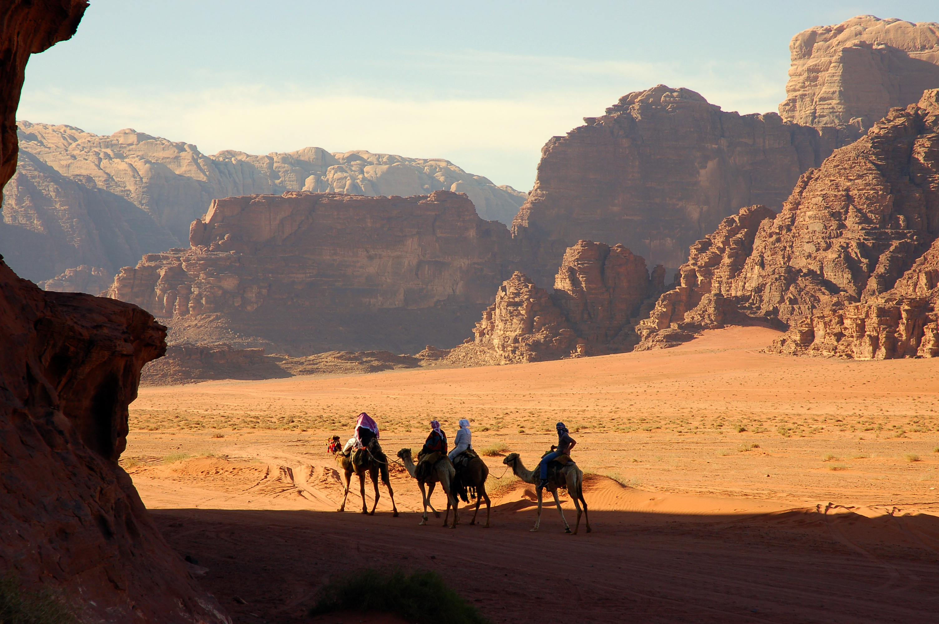Rejsende på kamelryggen udforsker den fascinerende Wadi Rum ørken i Jordan med dramatiske røde sandstensklipper