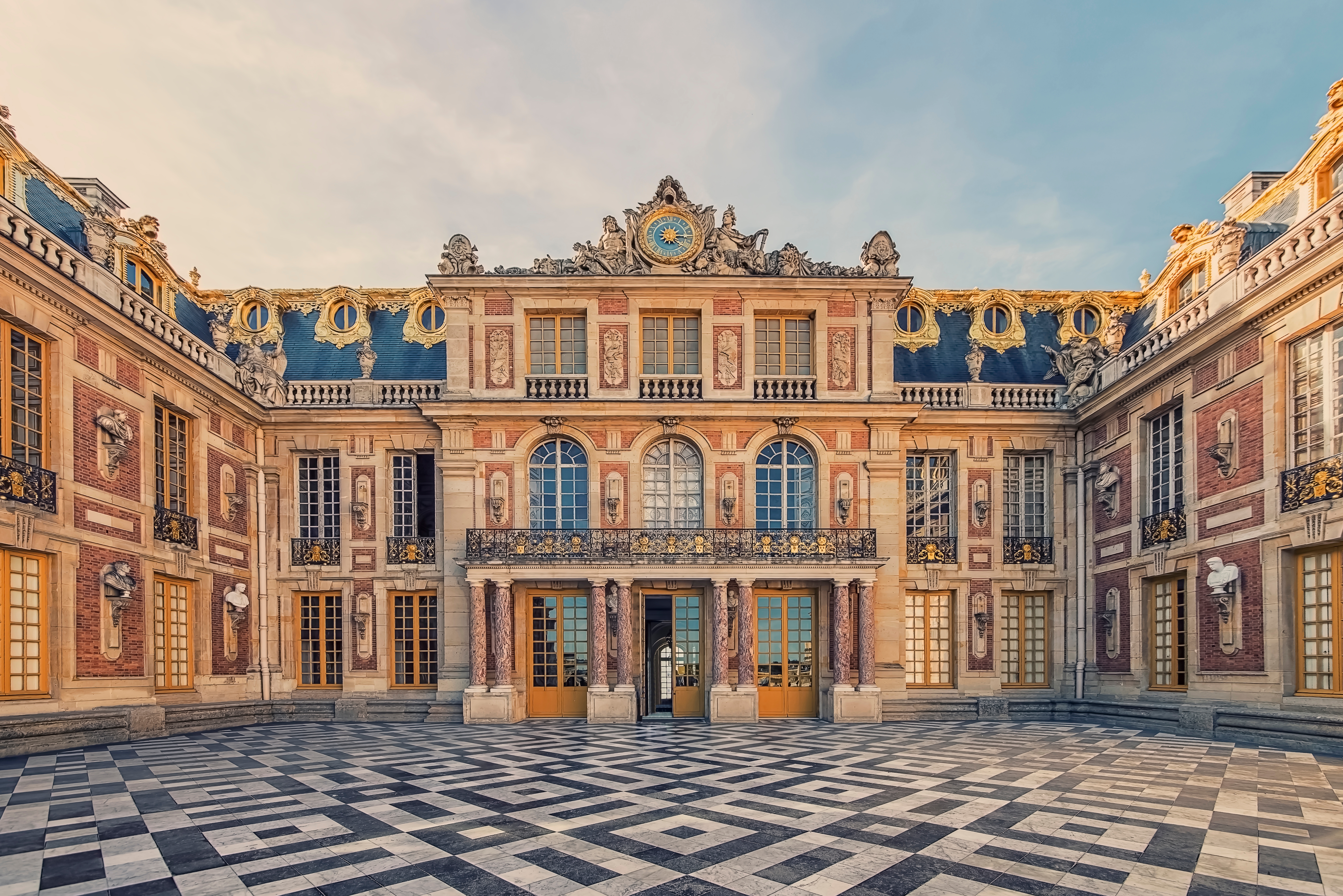 Versailles-slottets storslåede gård med det karakteristiske skakternede marmorgulv og den overdådigt udsmykkede barokfacade i Frankrig
