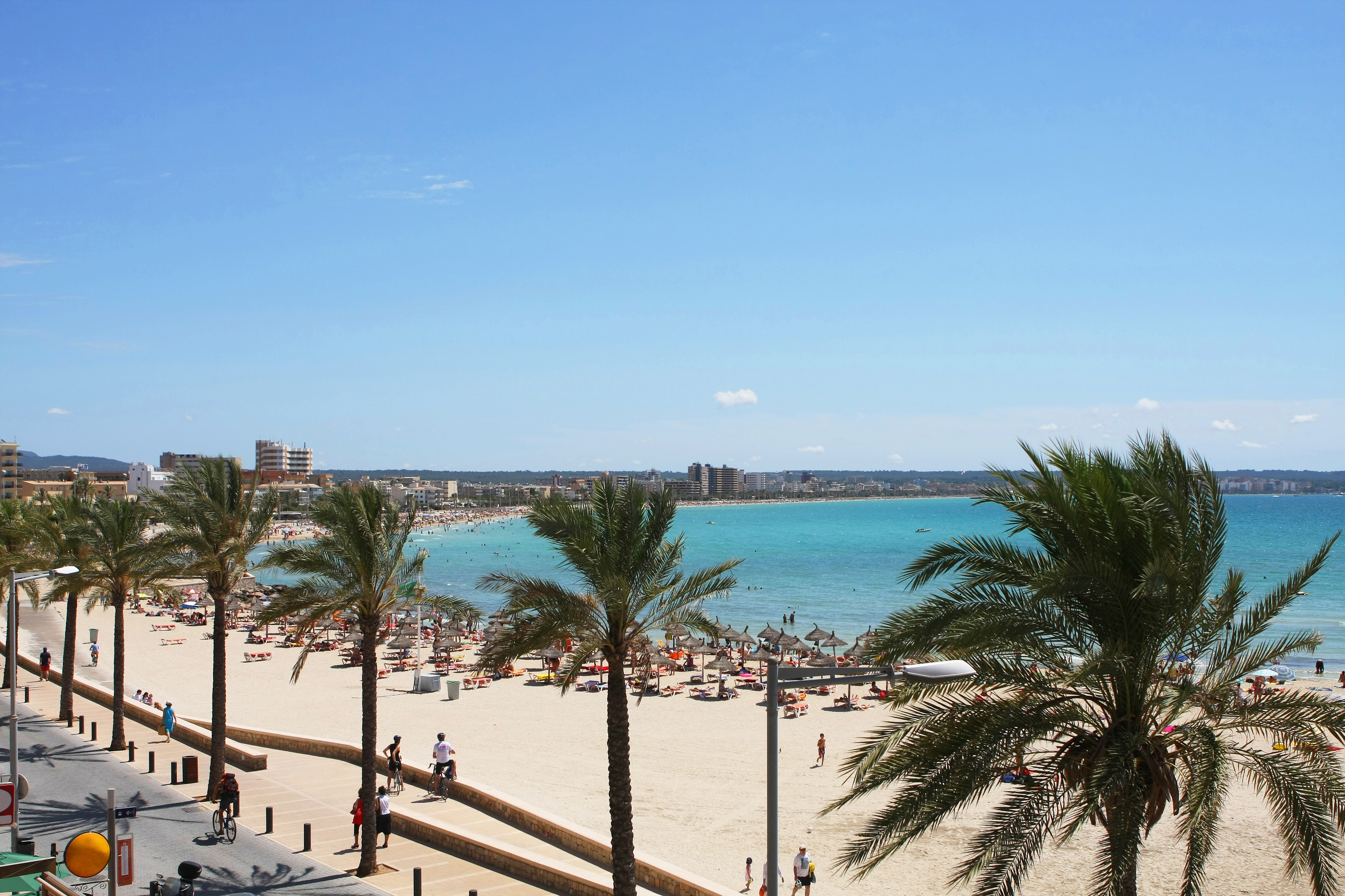 Playa de Palma på Mallorca med palmer, sandstrand og badegæster under blå himmel