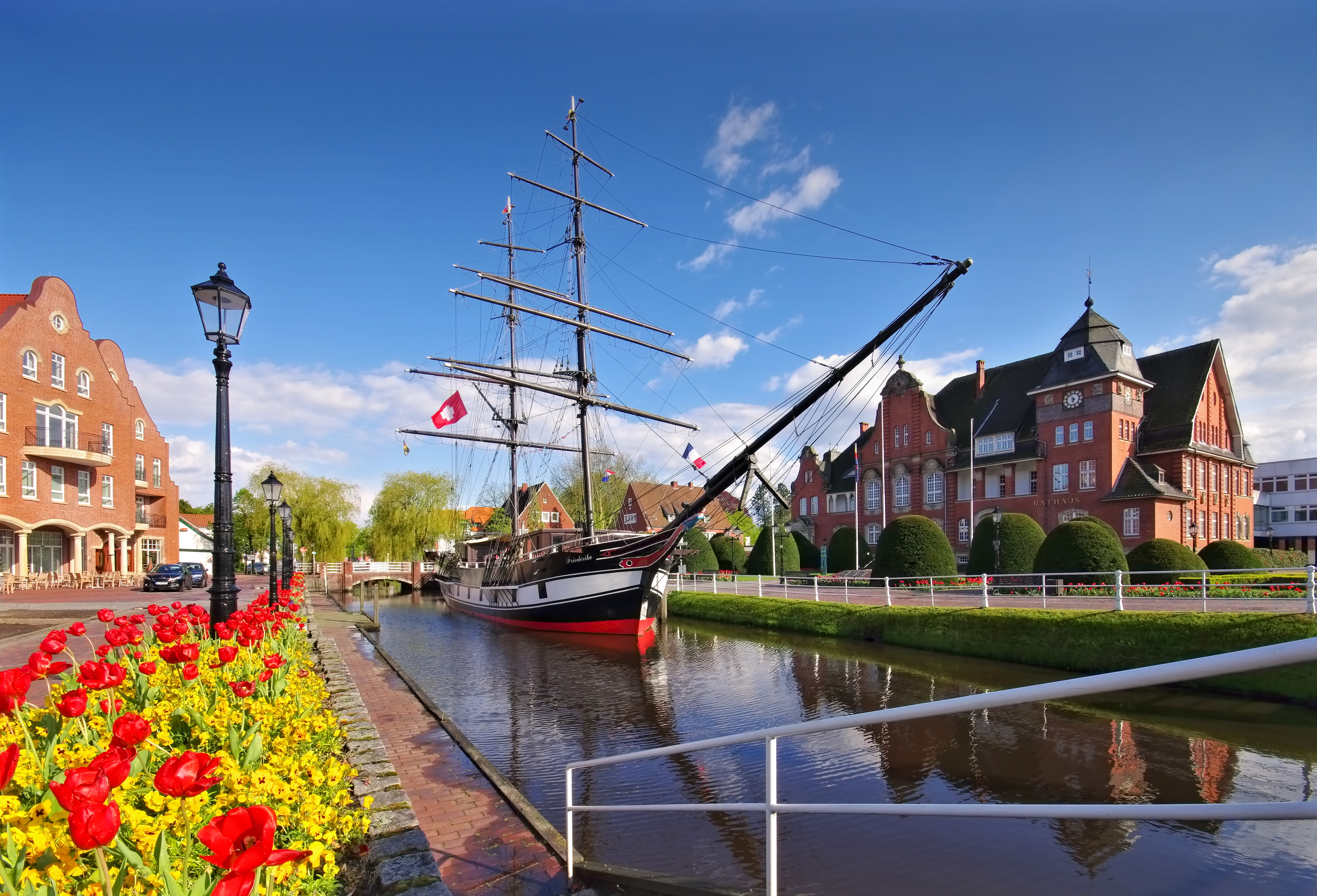 Romantisk forårsstemning i Papenburg med historisk sejlskib fortøjet ved kanalen og smukke røde tulipaner i forgrunden