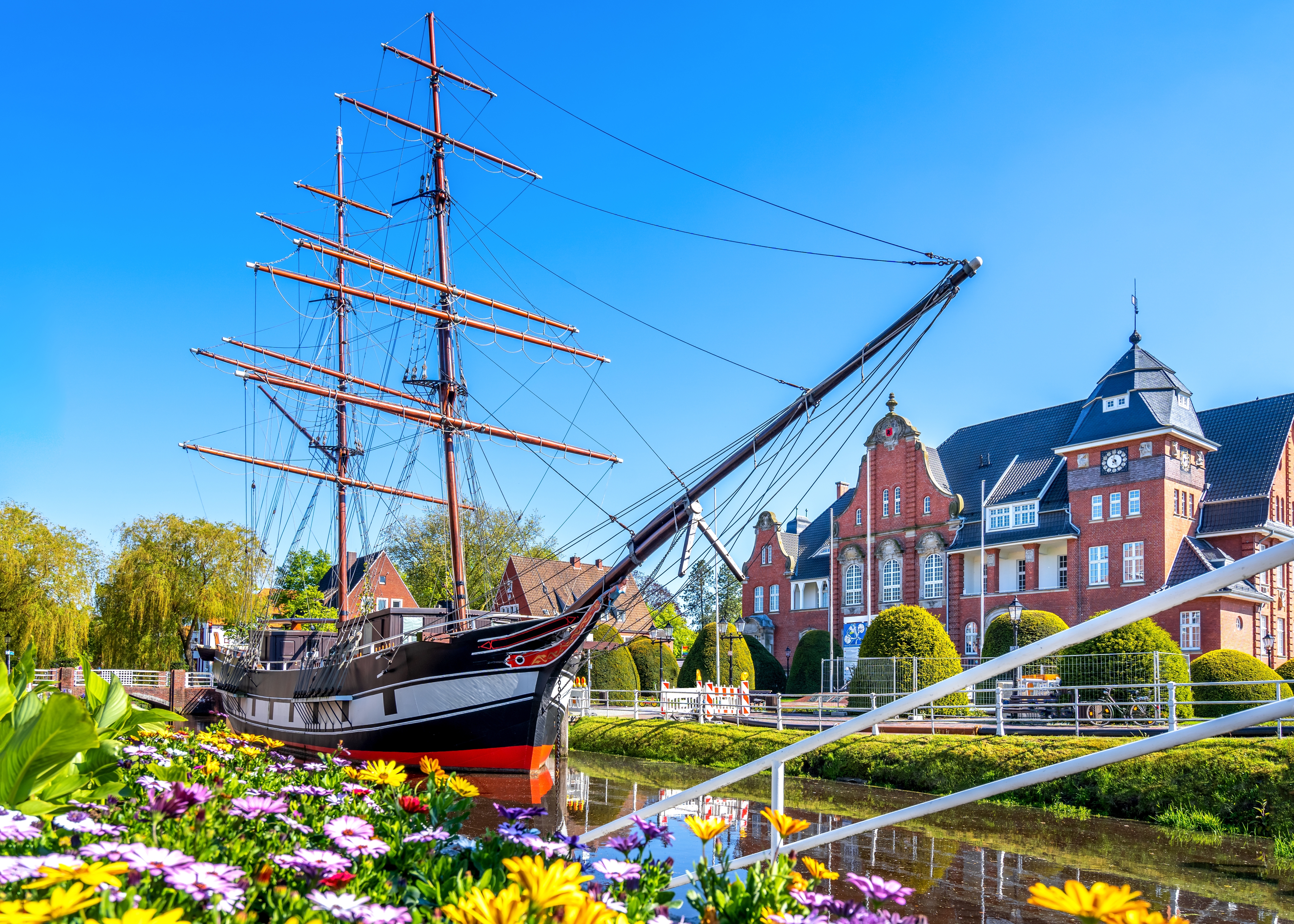 Malerisk udsigt over Papeburgs kanal med det historiske sejlskib Friederike og det røde rådhus omgivet af smukke forårsblomster i Østfrisland, Tyskland
