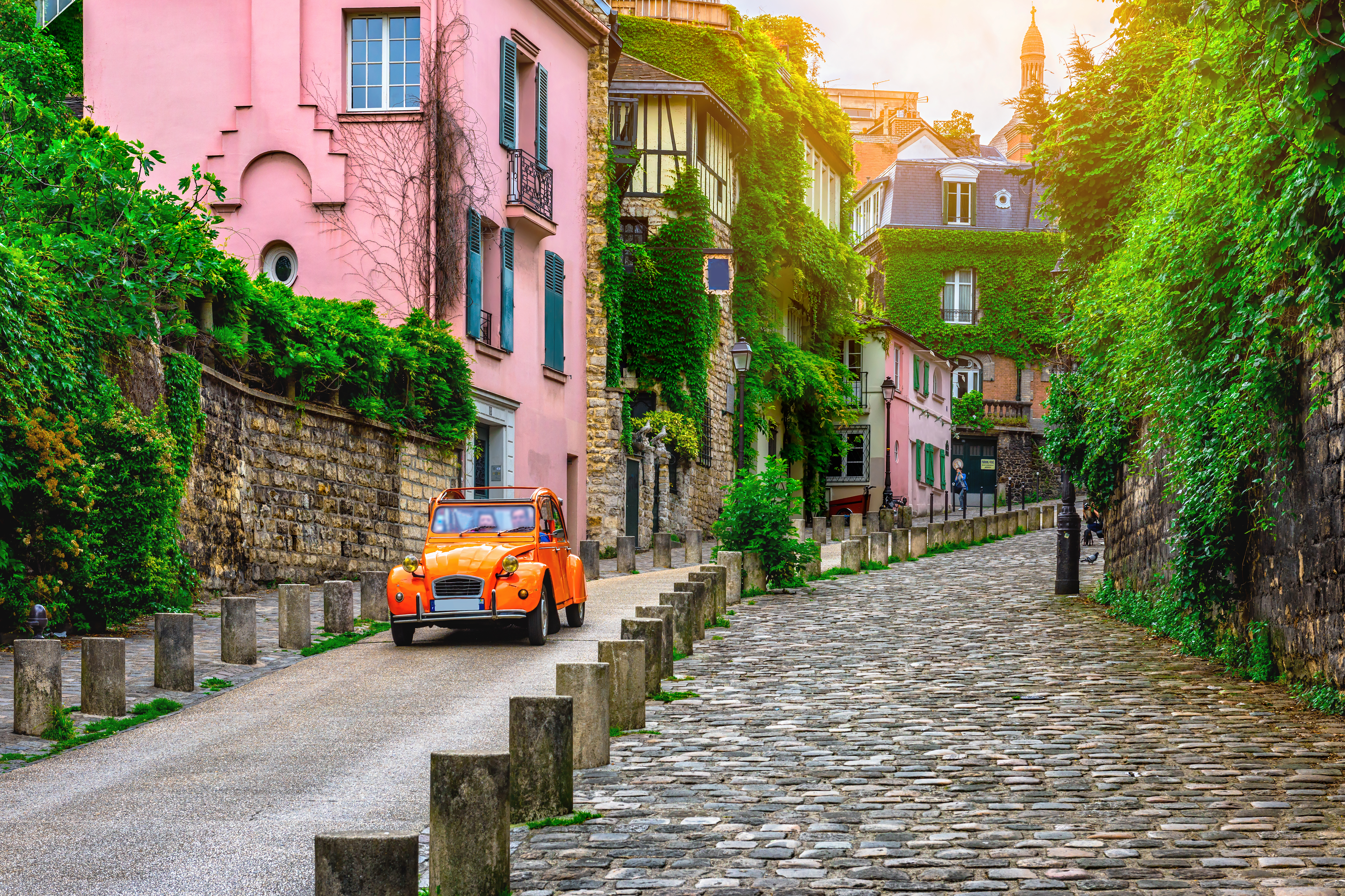 Klassisk parisisk brostensbelagt gade med vintage orange bil og traditionelle franske bygninger ved solnedgang