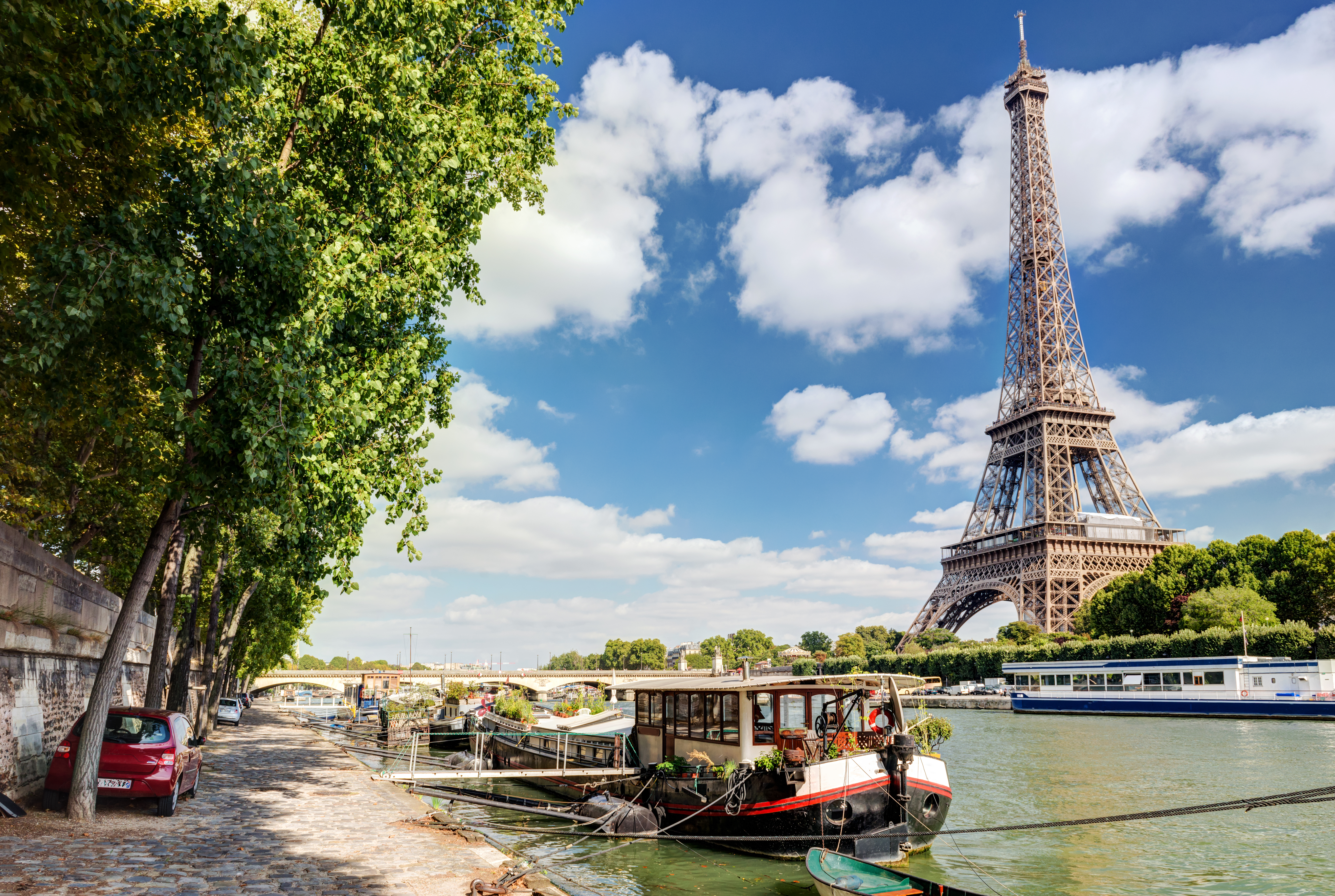 Smuk sommerudsigt over Paris med det majestætiske Eiffeltårn og farverige husbåde på Seinen