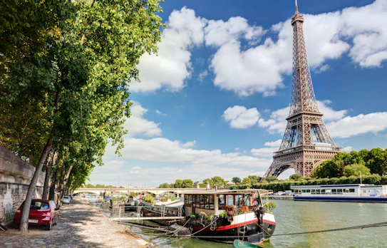 Smuk sommerudsigt over Paris med det majestætiske Eiffeltårn og farverige husbåde på Seinen