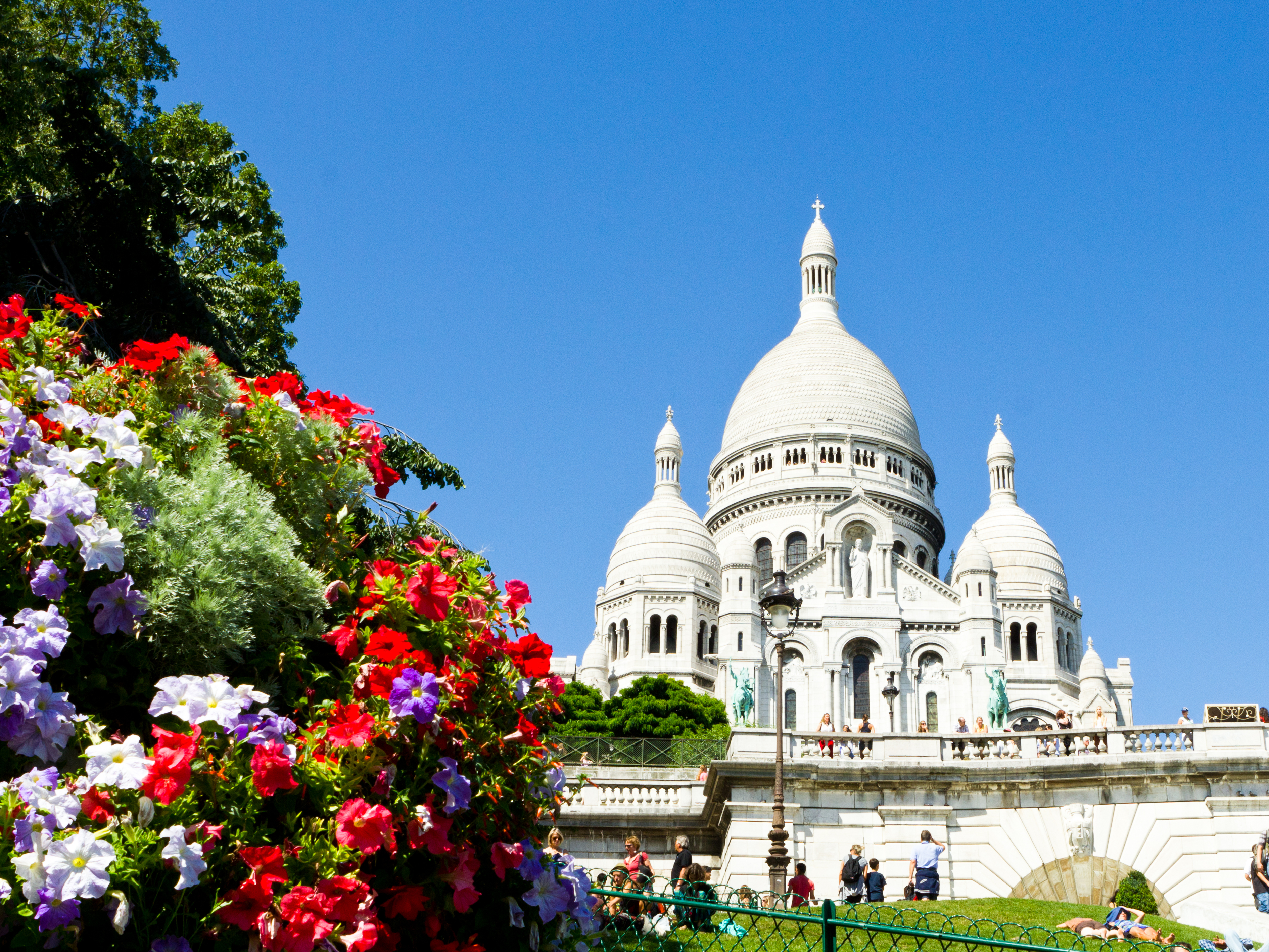 Den ikoniske Sacre-Coeur Basilika med sine hvide kupler troner på Montmartre i Paris, omgivet af farverige blomsterbede