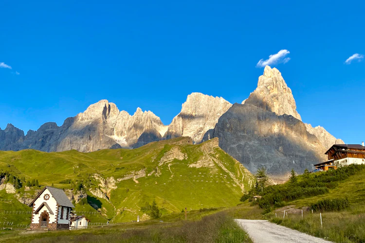 Fantastisk udsigt over Dolomitterne ved Passo Rolle med de ikoniske Pale di San Martino klippetinder, grønne alpenge og en charmerende bjergkirke i Trentino Alto Adige, Italien