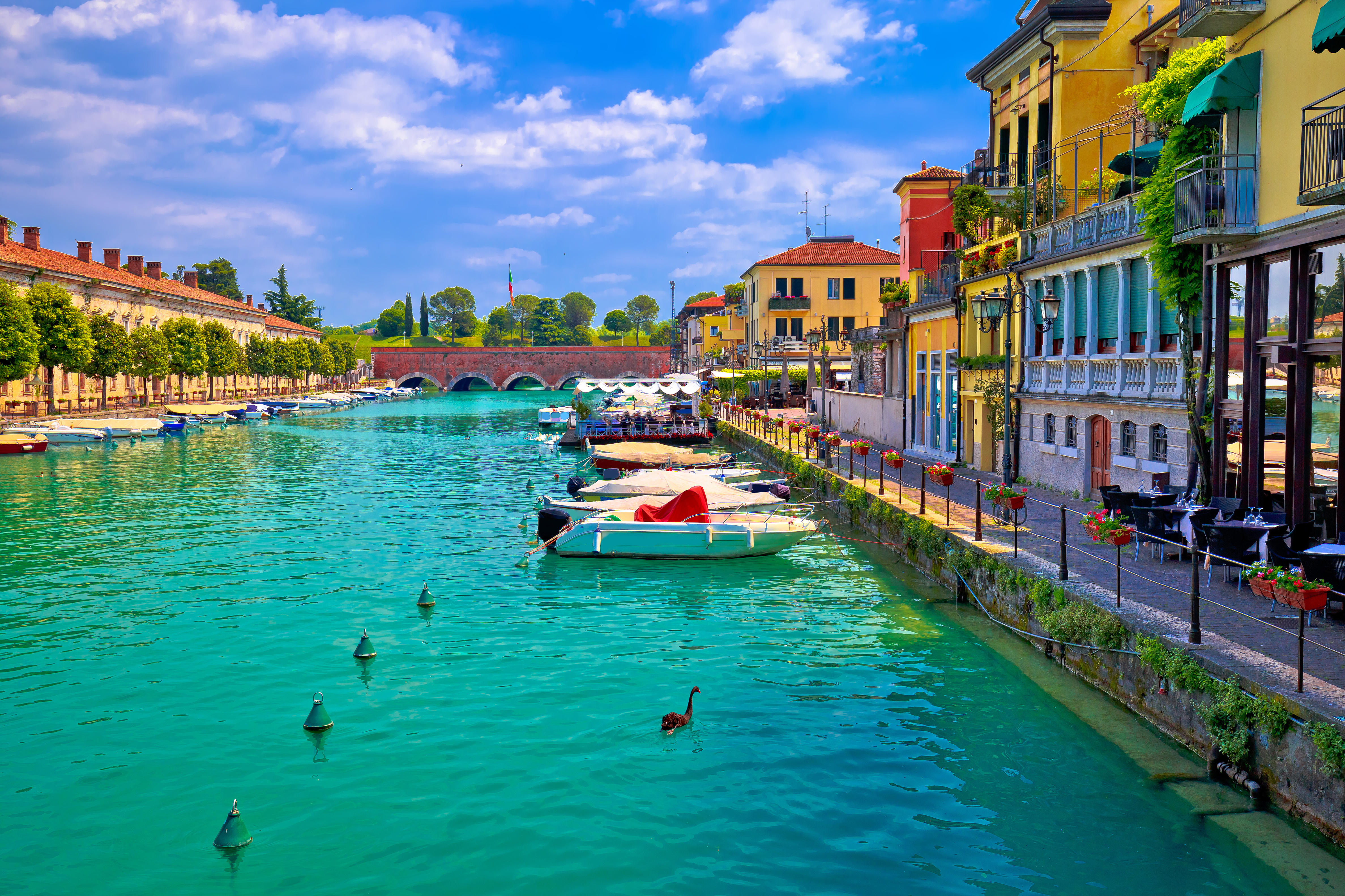 Venetiansk inspireret arkitektur i Peschiera del Garda med turkisblåt vand og traditionelle både