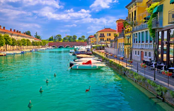Venetiansk inspireret arkitektur i Peschiera del Garda med turkisblåt vand og traditionelle både