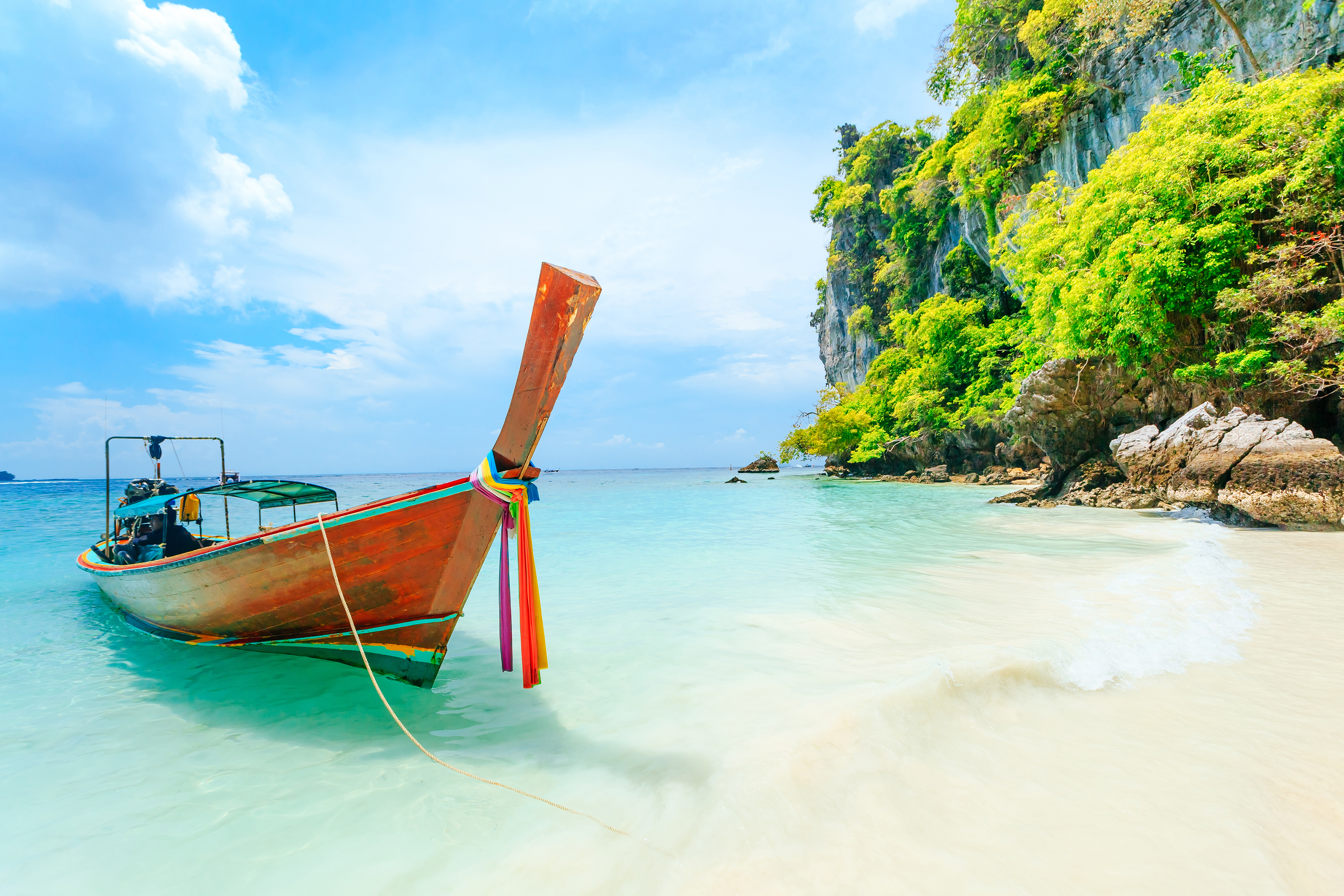 Idyllisk strand i Phuket med traditionel thai båd og turkisblåt vand