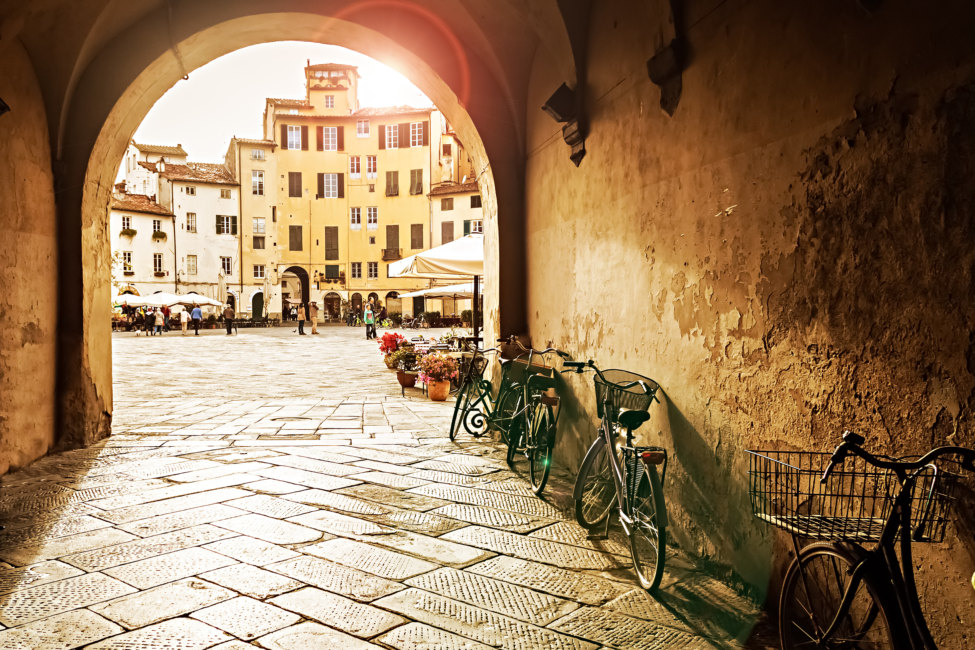 Den smukke Piazza dell'Anfiteatro i Lucca ved solnedgangstid, hvor det varme lys fremhæver de gule bygninger der omkranser den ovale plads bygget på et romersk amfiteater