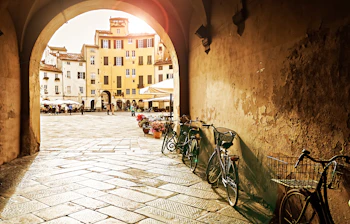 Den smukke Piazza dell'Anfiteatro i Lucca ved solnedgangstid, hvor det varme lys fremhæver de gule bygninger der omkranser den ovale plads bygget på et romersk amfiteater