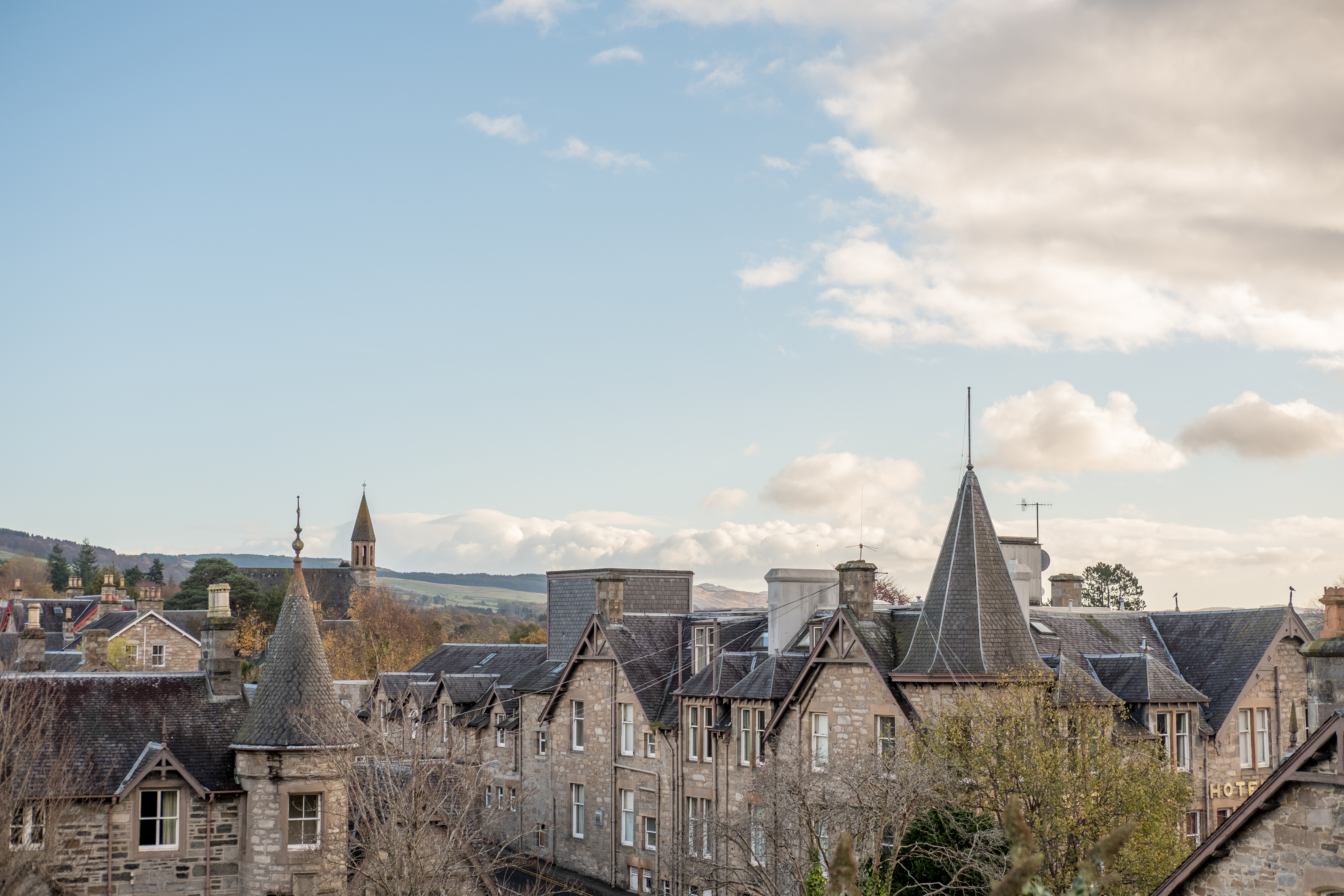 Idyllisk bybillede af Pitlochry i Perthshire, Skotland, med charmerende stenbygninger og tårne mod en blå himmel med spredte skyer