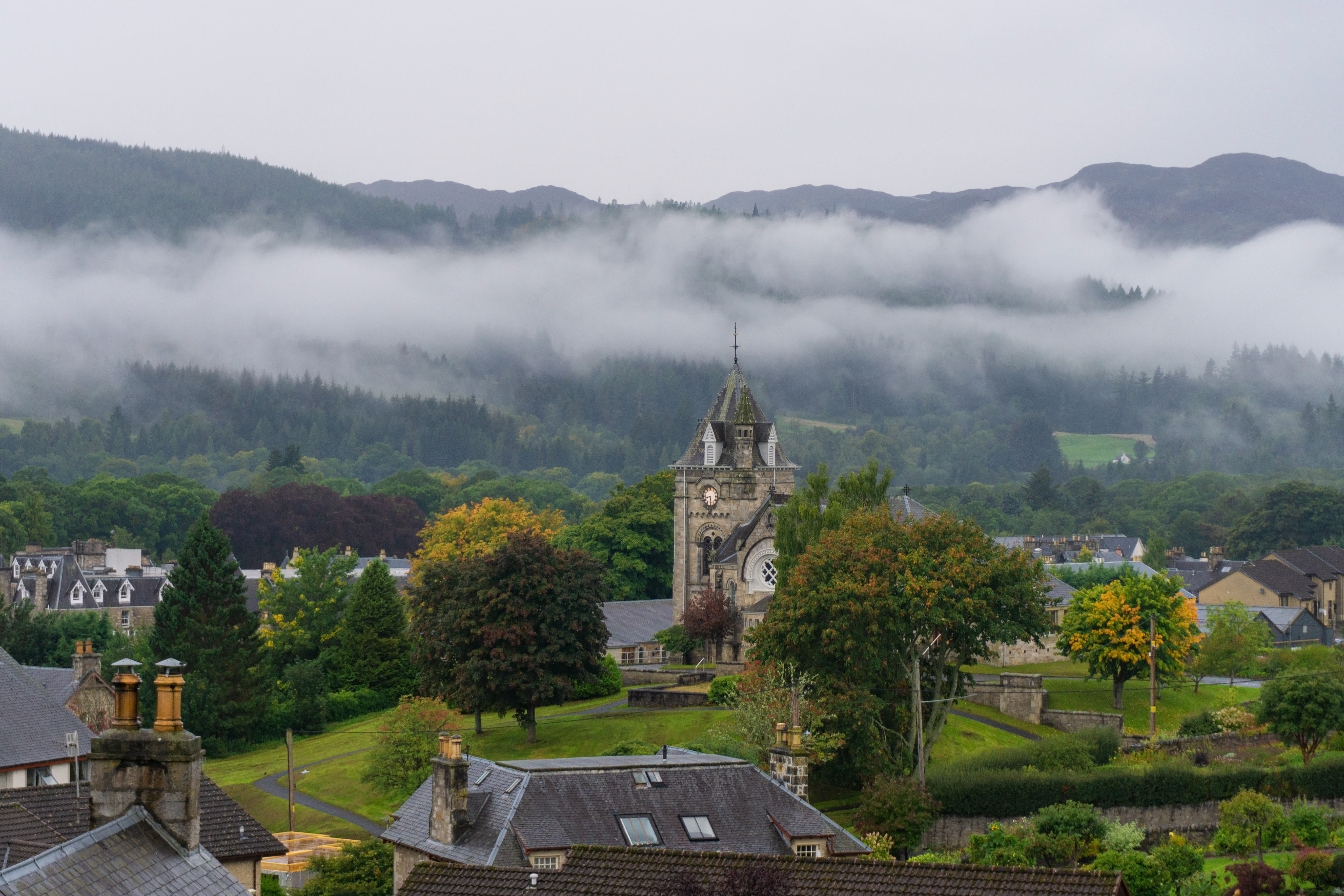 Idyllisk udsigt over Pitlochry med Pitlochry Parish Church og tågedækkede skotske højlandsbjerge omgivet af grønne skove