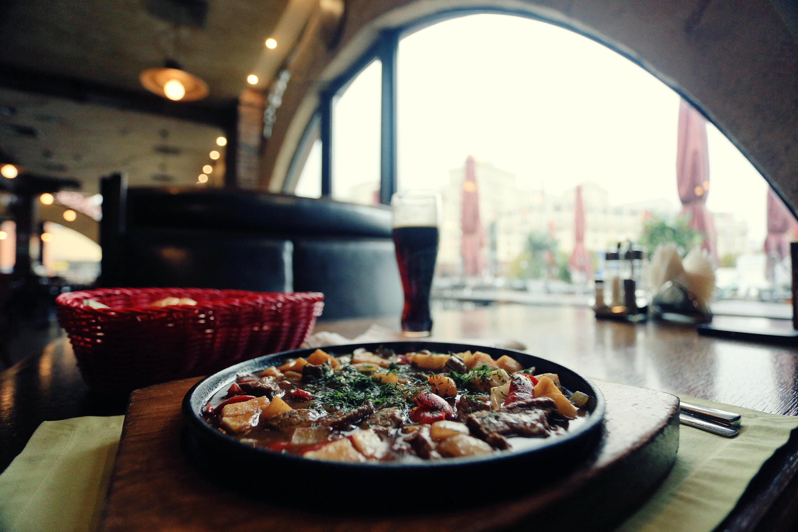 Varm pizza med varierede toppings på sort tallerken i restaurant med byudsigt