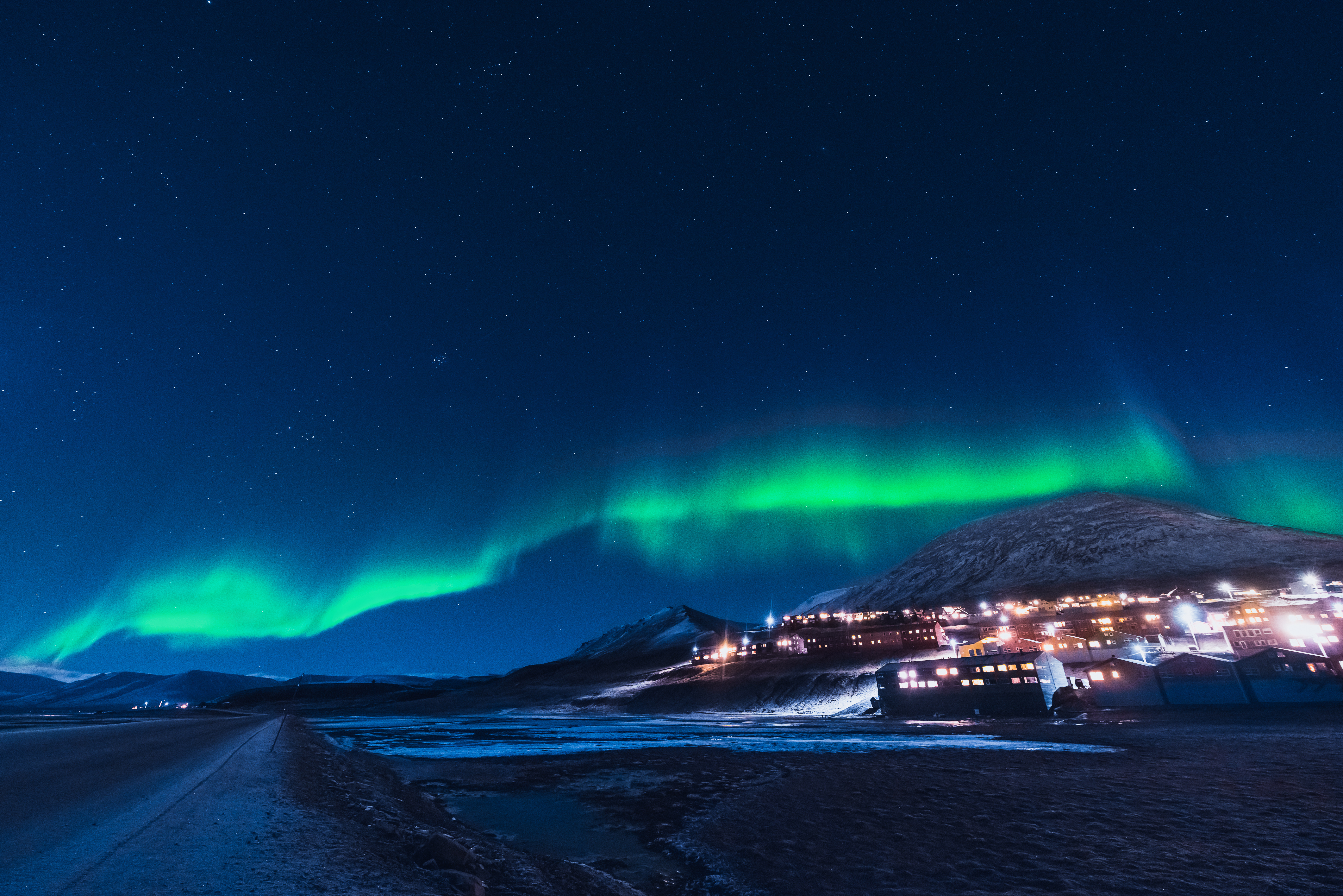 Fantastiske nordlys i grønne bølger over arktisk bjerglandskab med bebyggelse