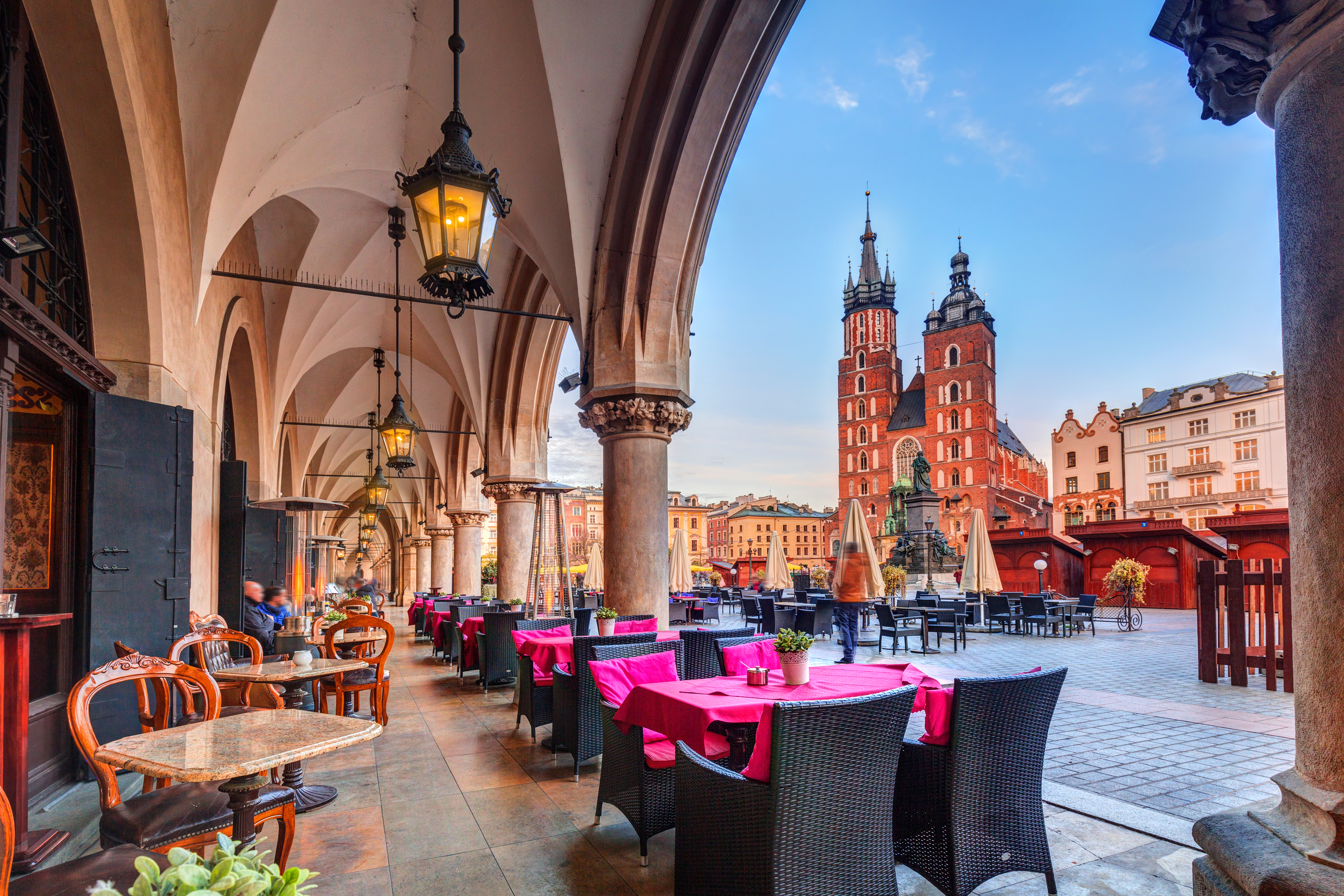 Elegante restaurantborde under historiske arkader med udsigt til Krakows berømte kirketårne