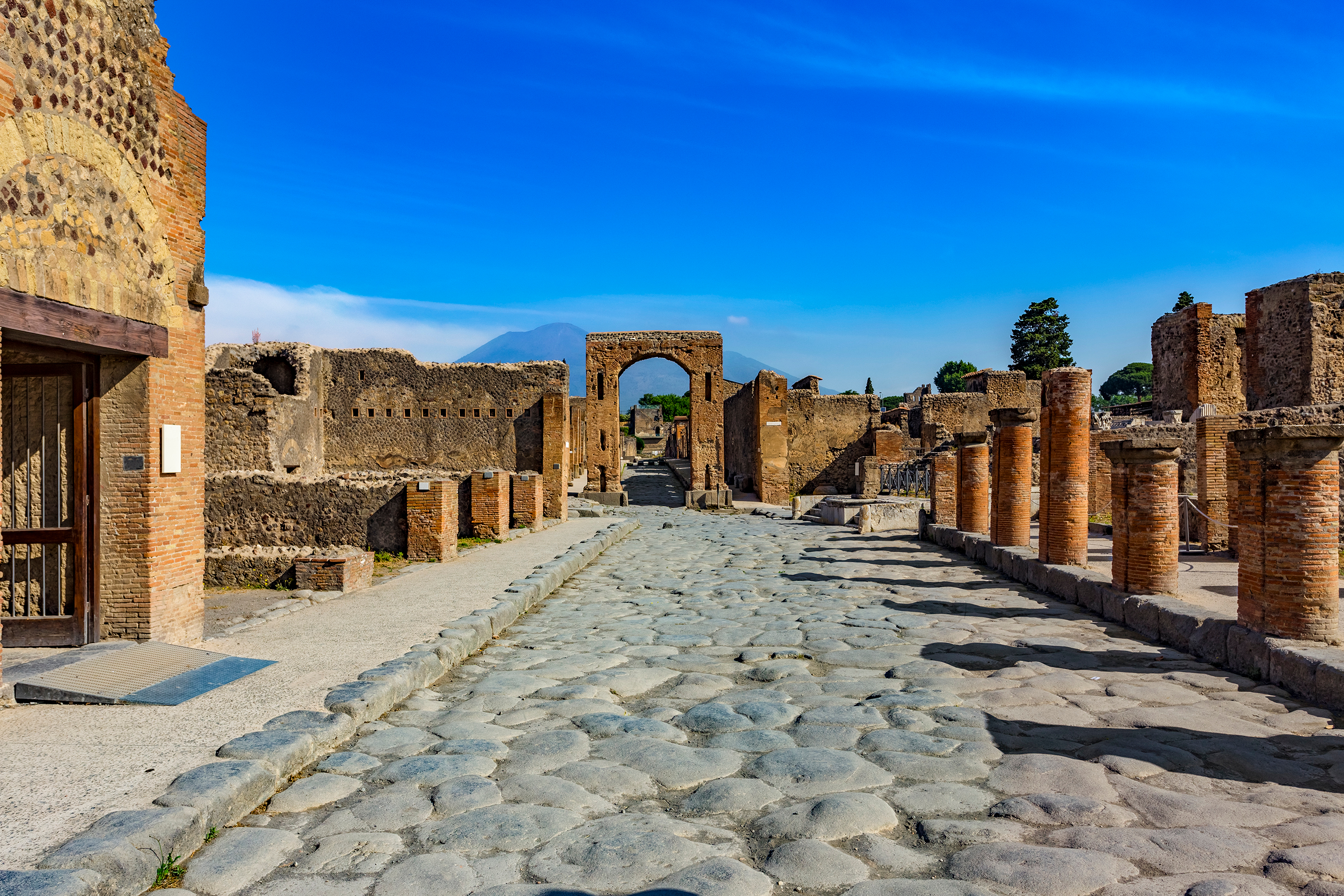 Brolagte gader og romerske søjler i Pompeii med Caligulas triumfbue og Vesuv i horisonten, Campania, Italien