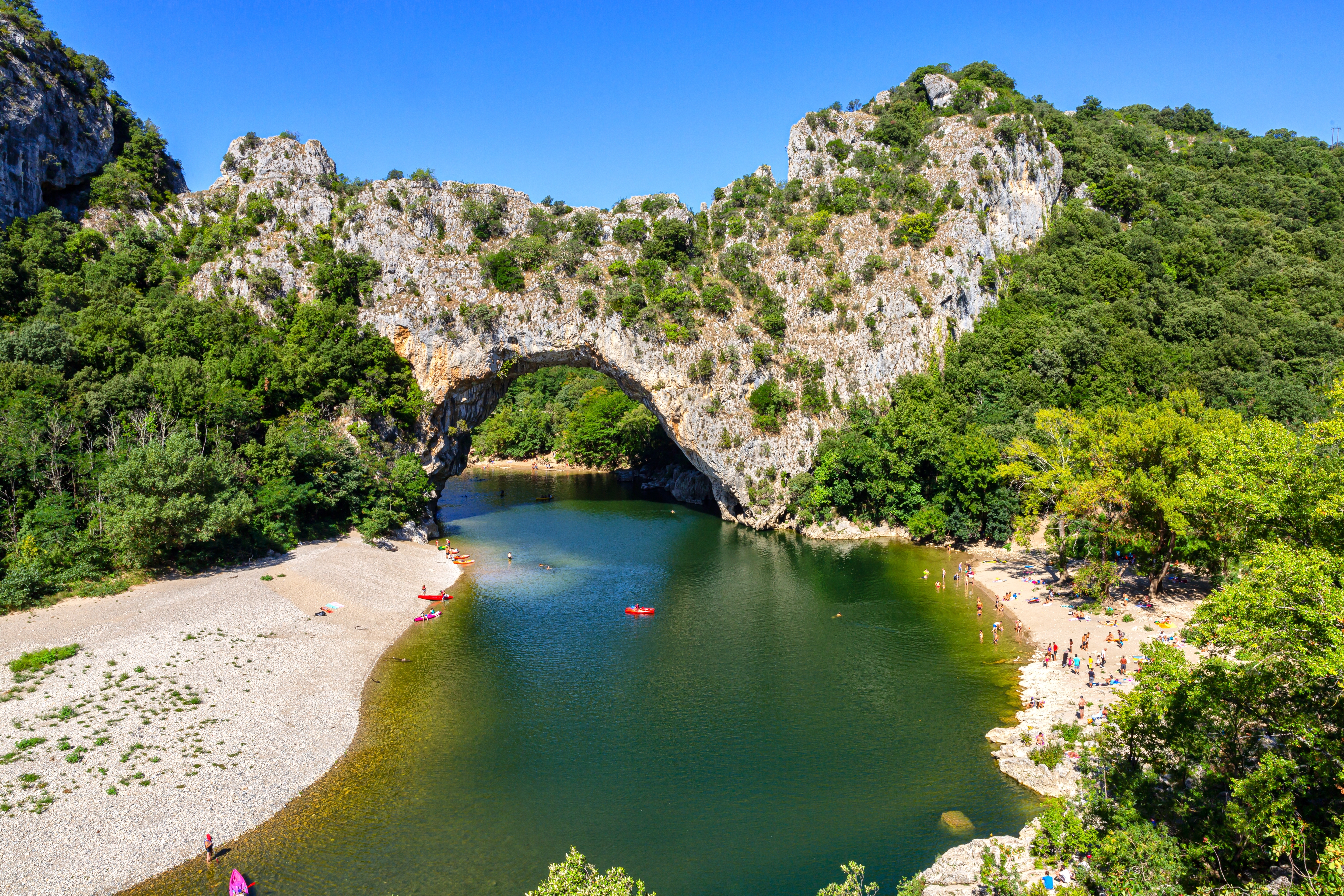 Naturskøn udsigt over Pont d'Arc og Ardèche-floden i Frankrig, hvor turister nyder sol og aktiviteter ved det smukke grønne vand