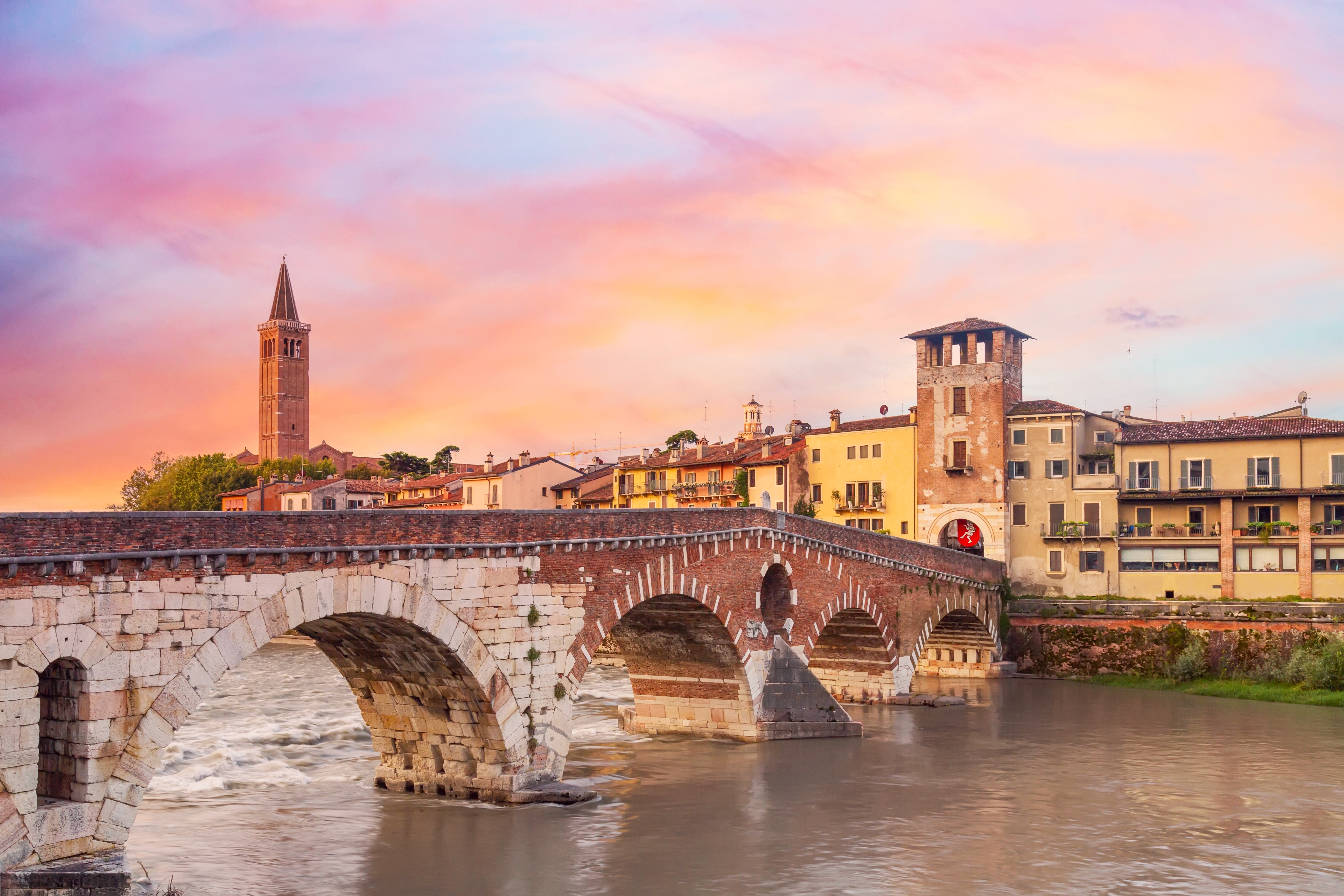 Romantisk solopgang over Ponte di Pietra broen i Verona med historiske bygninger og kirketårn i baggrunden