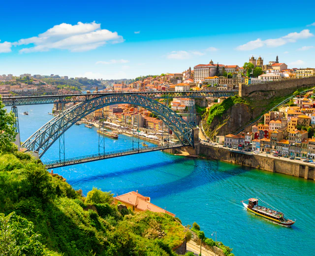 Stemningsfuld udsigt over Portos historiske bymidte med den ikoniske jernbro over Douro-floden, terrasserede huse i varme farver og traditionel båd