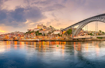 UNESCO-beskyttet kulturarv i Porto med den berømte Dom Luis bro, historiske bygninger og sejlbåde på Douro-floden i aftenlys