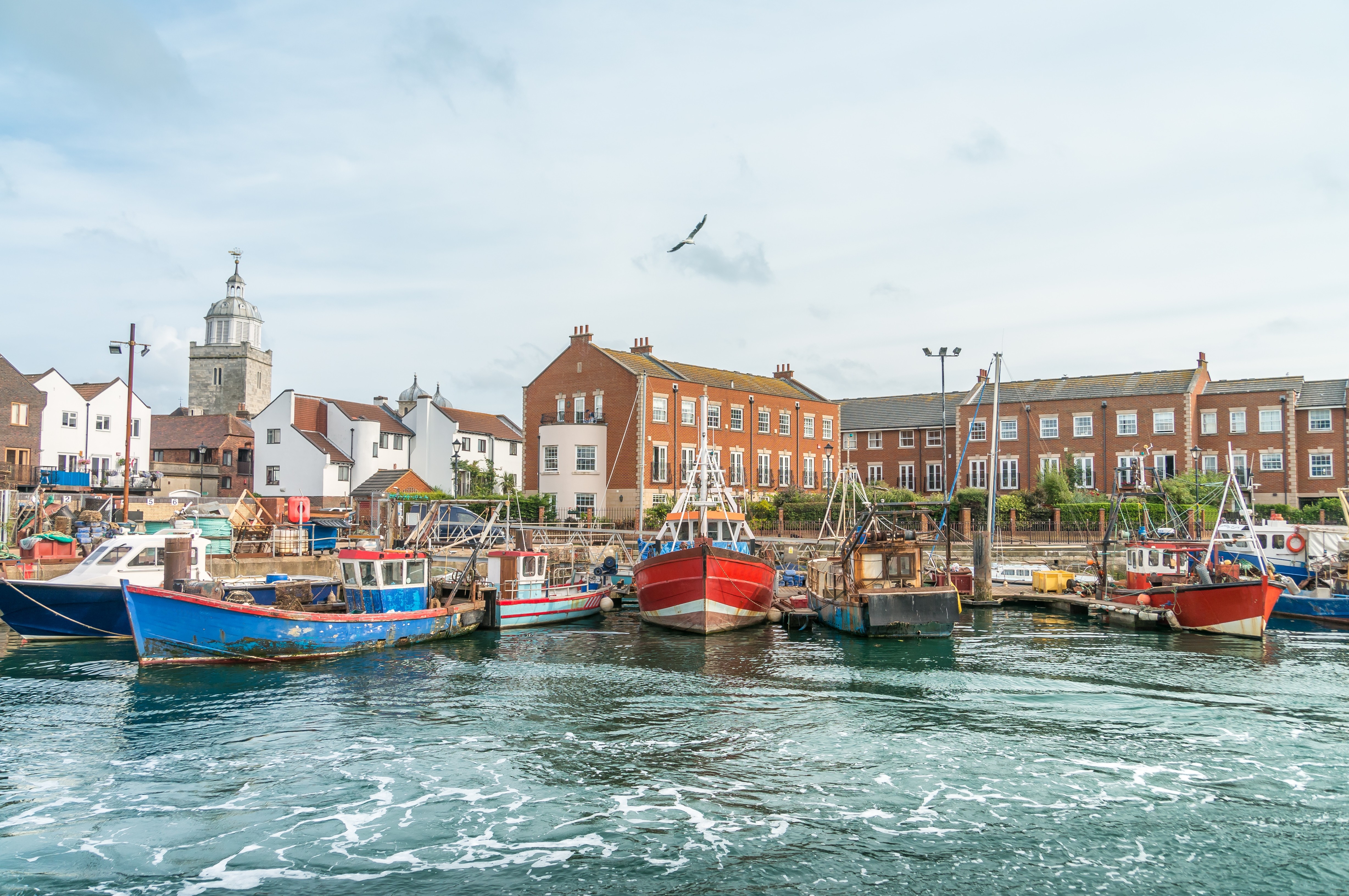 Tradtionelle fiskerbåde i blå og rød fortøjet i Portsmouth Harbour med georgiske huse langs havnepromenaden