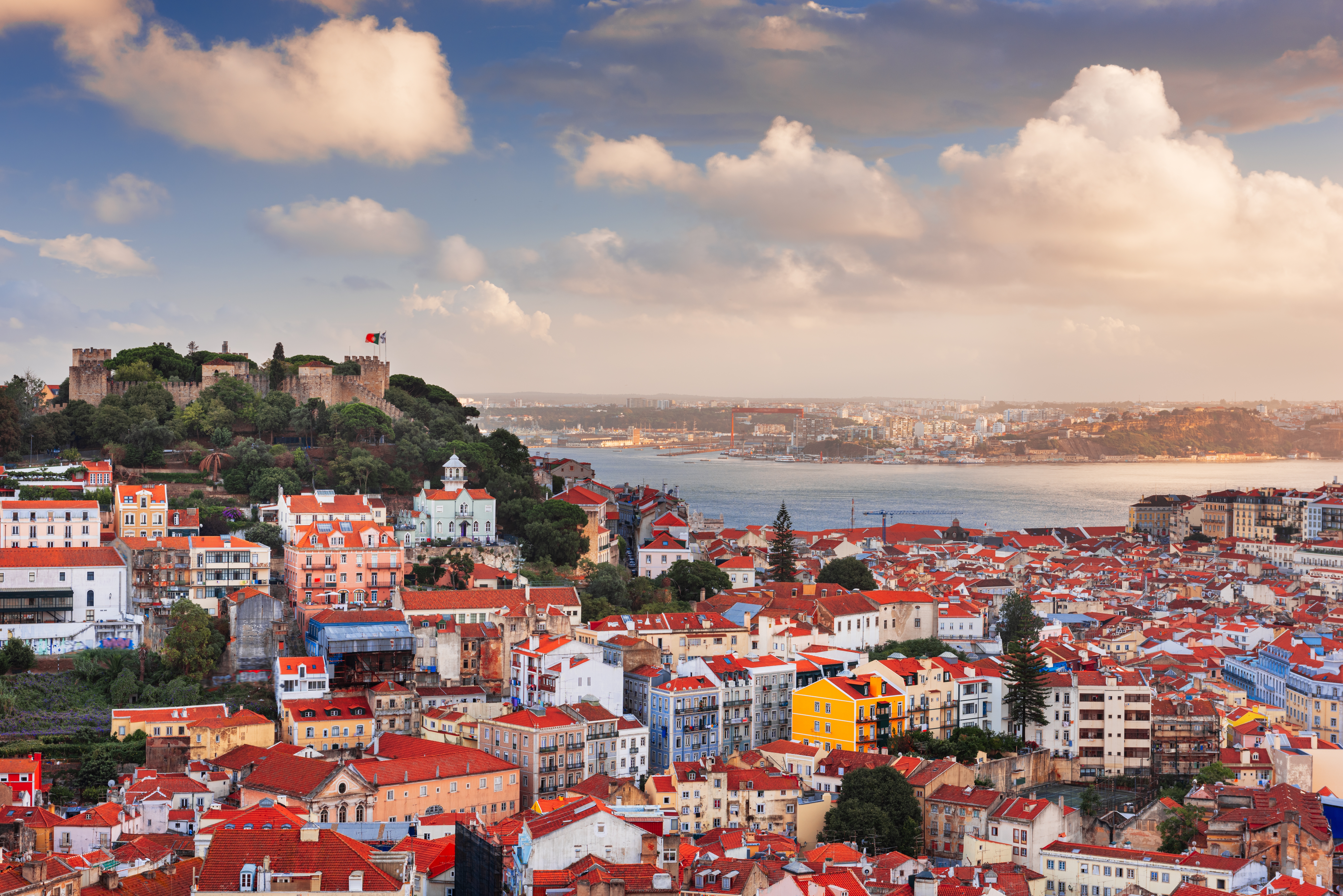 Idyllisk aftenudsigt over Lissabons historiske centrum med dens bakkede terræn og traditionelle portugisiske arkitektur oplyst af den gyldne solnedgang over Tagus-floden