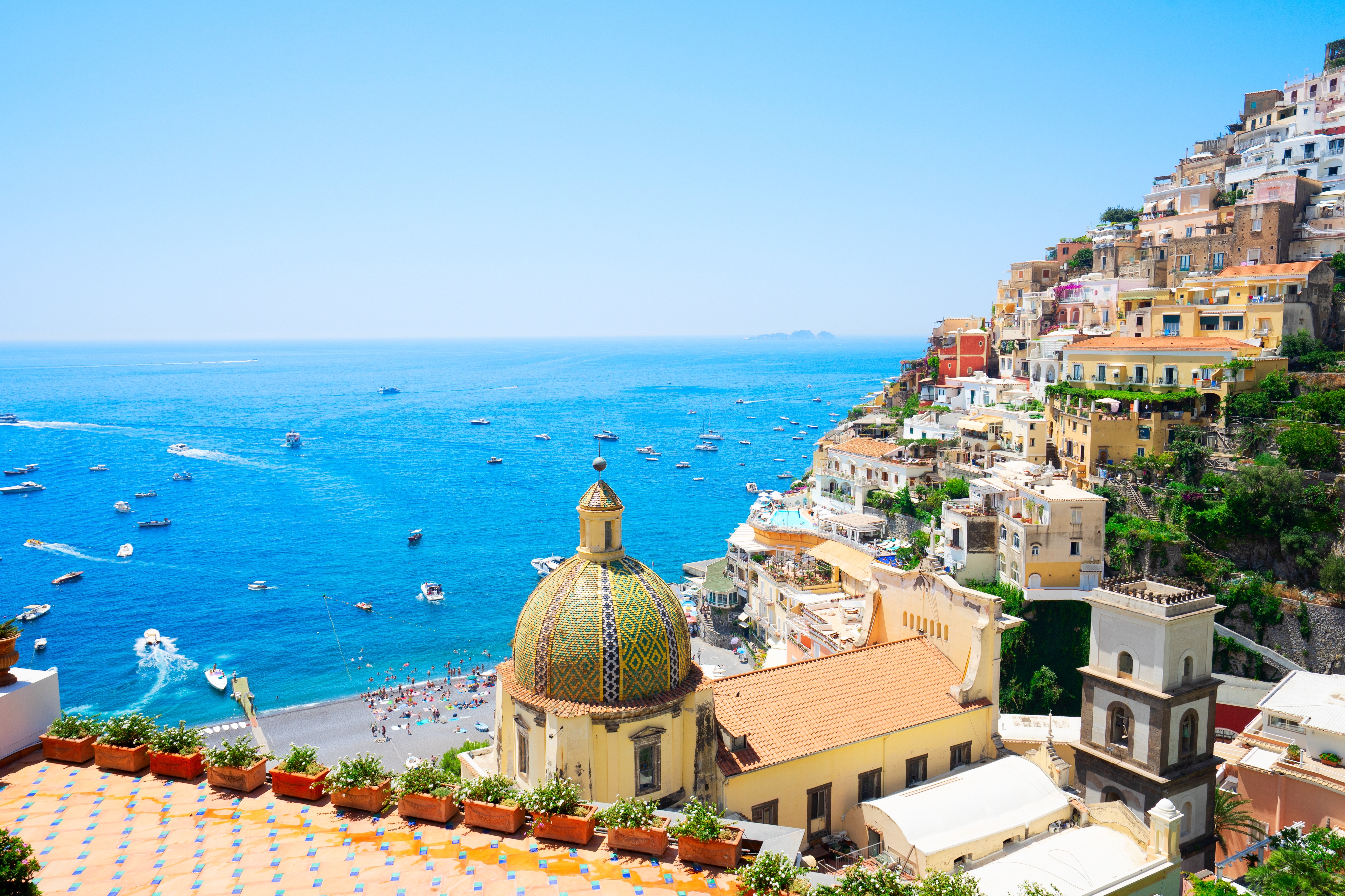 Det maleriske Positano på Amalfkysten i Italien med farverige huse bygget ind i klipperne, den smukke kirkedome og det blå Middelhav fyldt med både