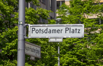 Hvide byskilte ved Potsdamer Platz i Berlin centrum med grønne træer omkring