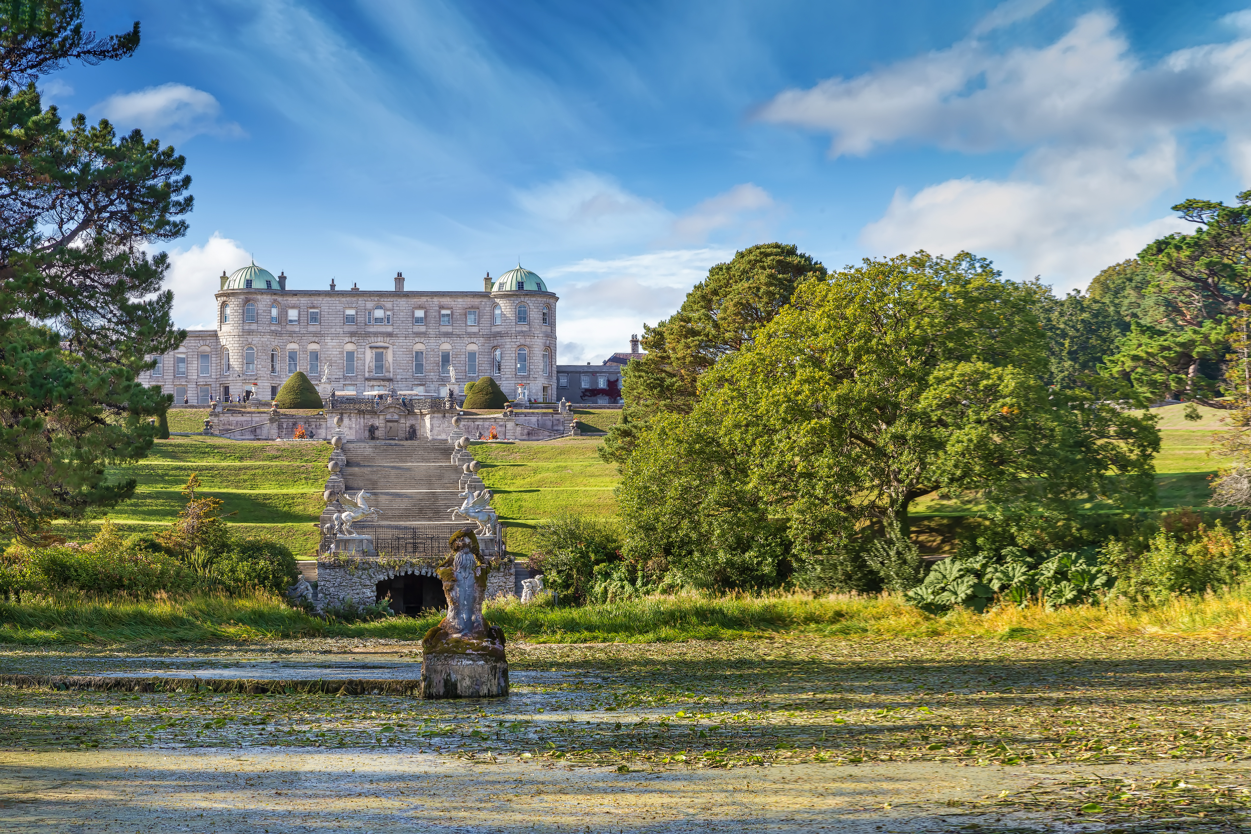 Magisk udsigt over Powerscourt Estate i Enniskerry, Irland, med det historiske herresæde, skulpturprydede havestier og en rolig sø dækket af åkander
