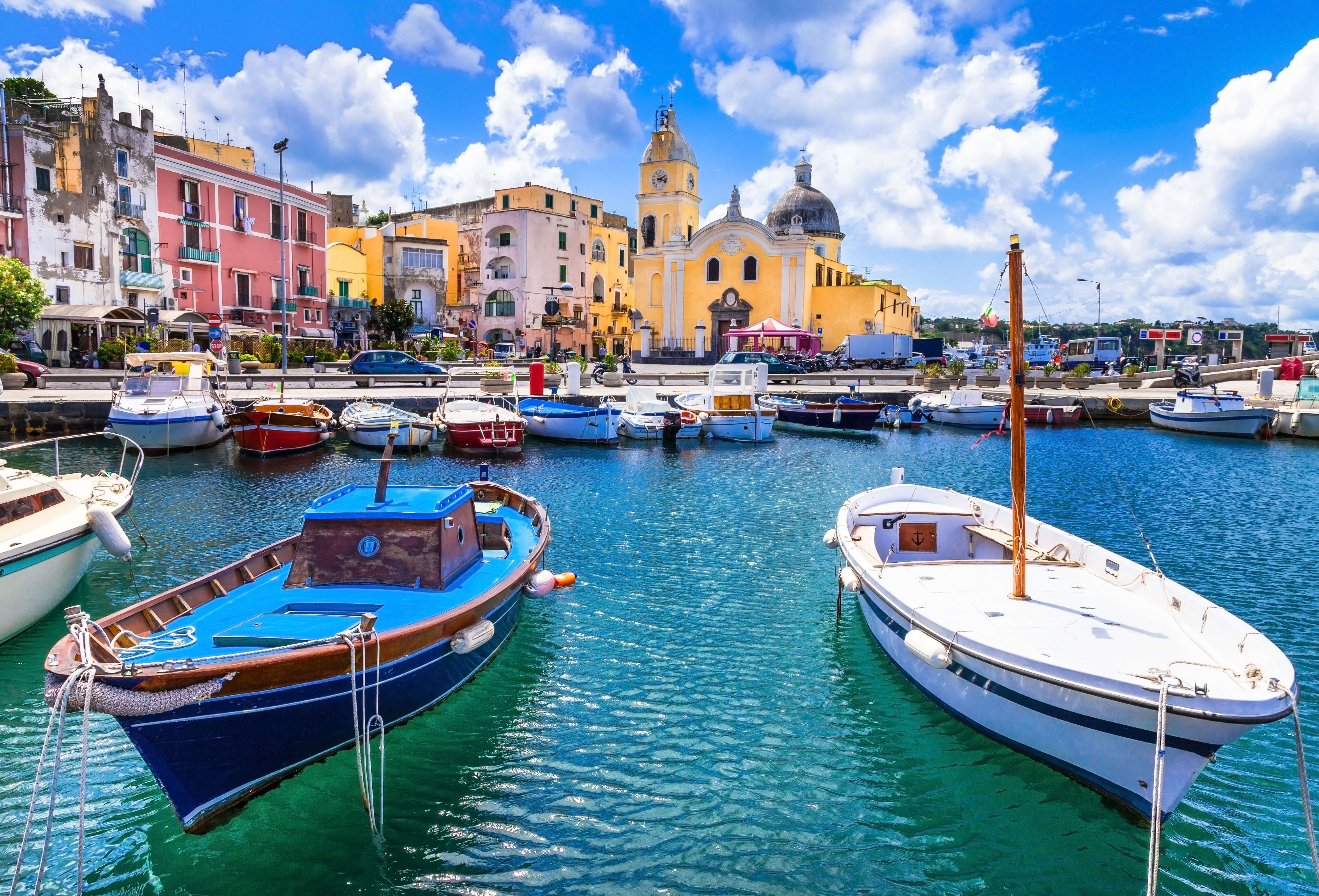 Smuk italiensk fiskerhavn på Procida med blå og hvide både, spejlblank turkis vand og charmerende farverige huse ved Middelhavet