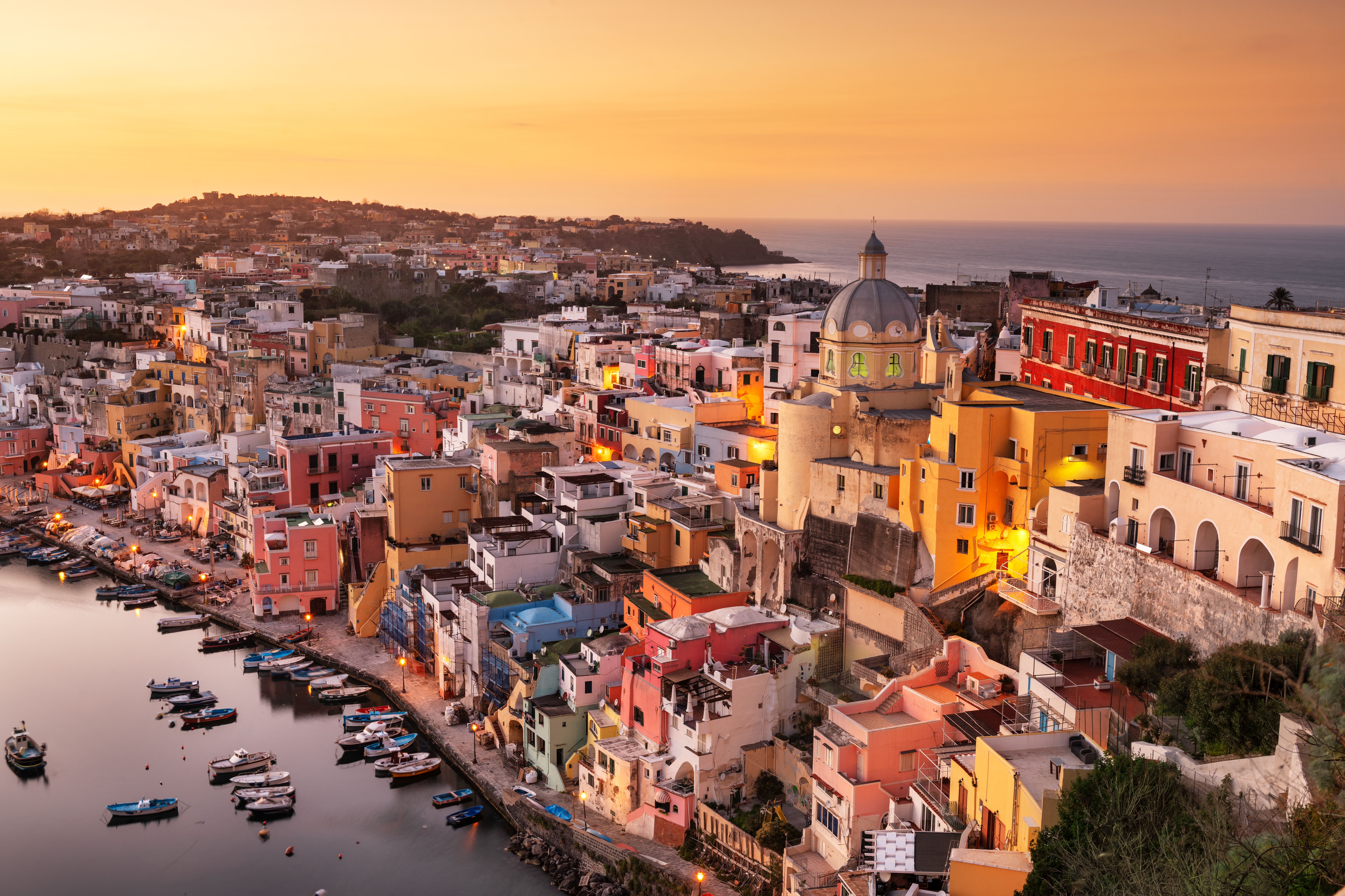 Magisk solnedgang over den historiske ø Procida med farverige bygninger, kirke og både i Napoli-bugten, Campania