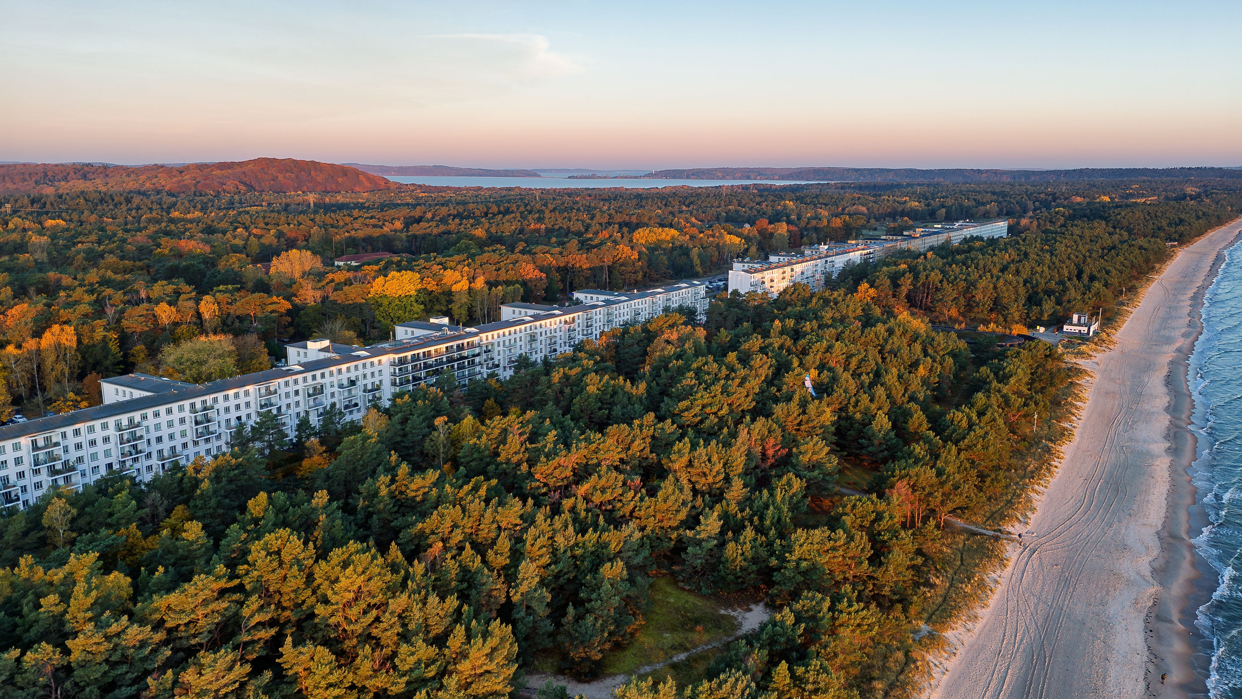 Luftudsigt over Proras berømte resort på Rügen med historisk bygningskompleks ved Østersøen omgivet af gylden efterårsskov ved solopgang
