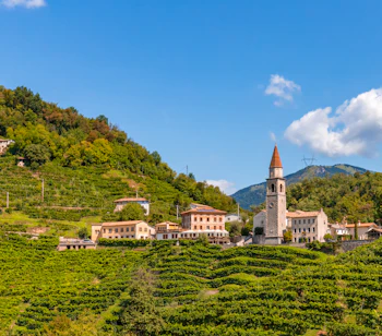 Terrasserede prosecco vingårde omkring historisk italiensk landsby med kirketårn i Valdobbiadene