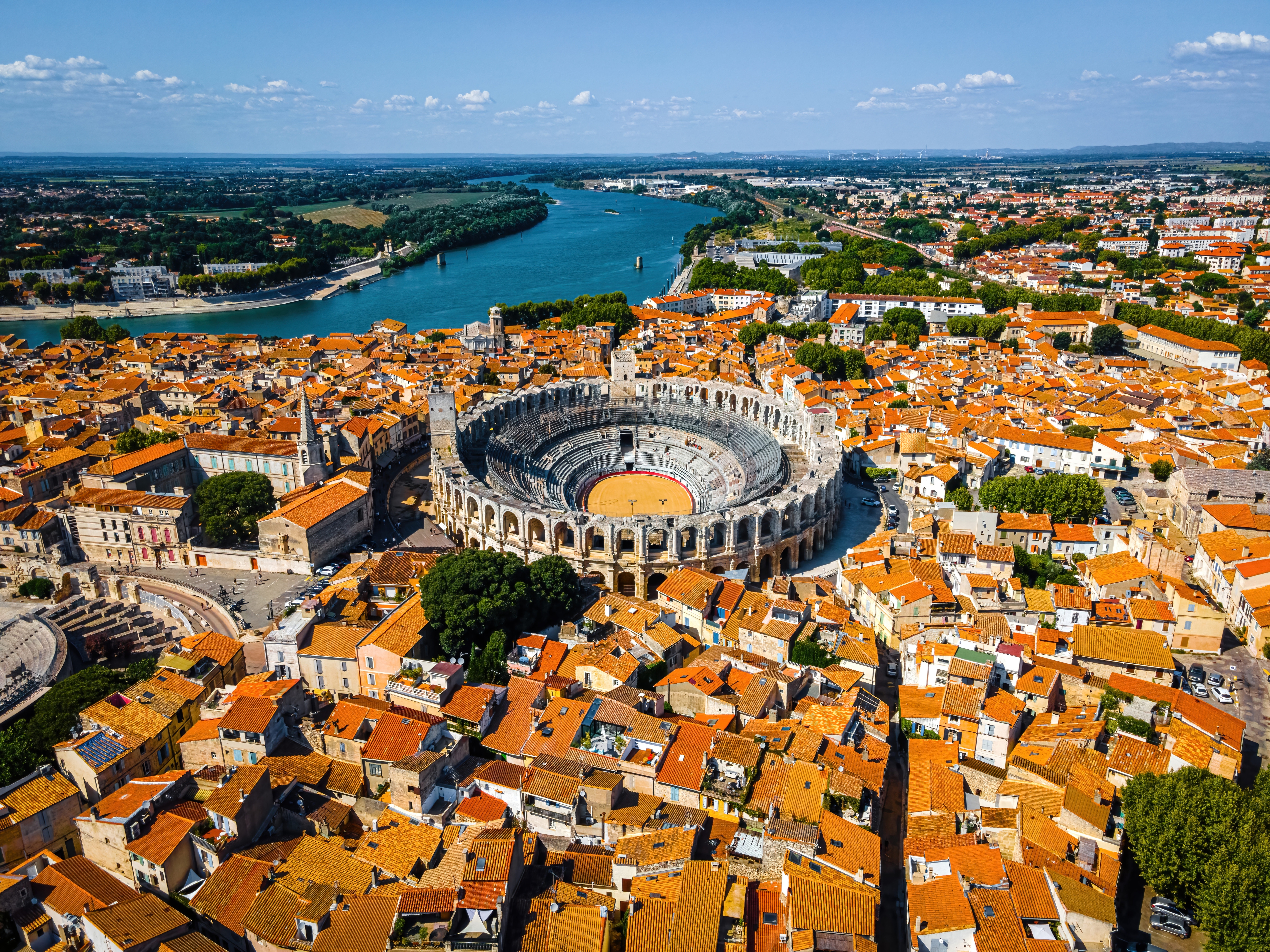 Imponerende fugleperspektiv af Arles med det antikke romerske amfiteater centralt placeret blandt de orange tage og Rhône-floden i Provence