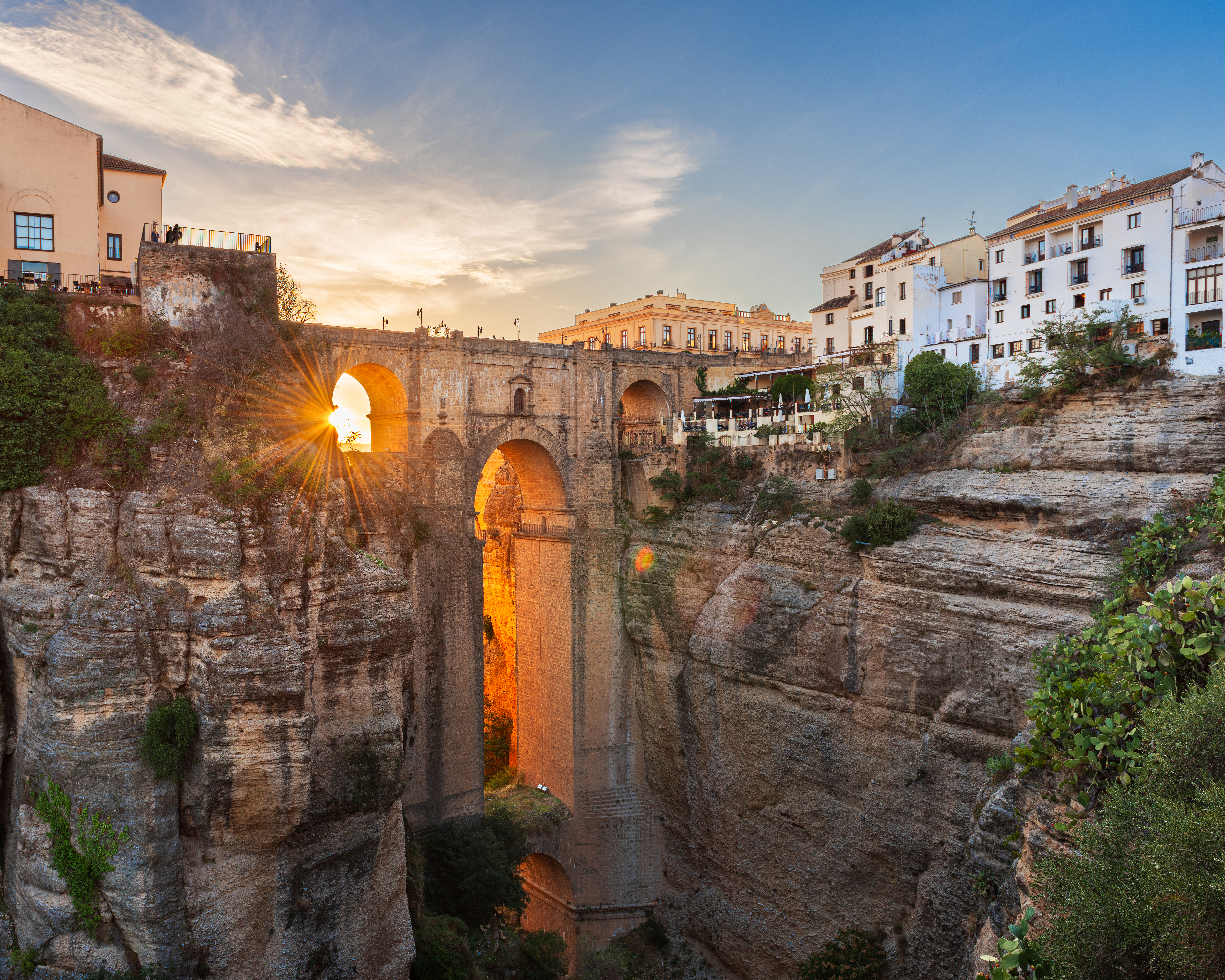 Aftensolen skinner gennem buerne på Puente Nuevo-broen i Ronda, Spanien, med dramatisk udsigt over El Tajo-kløften i Andalusien